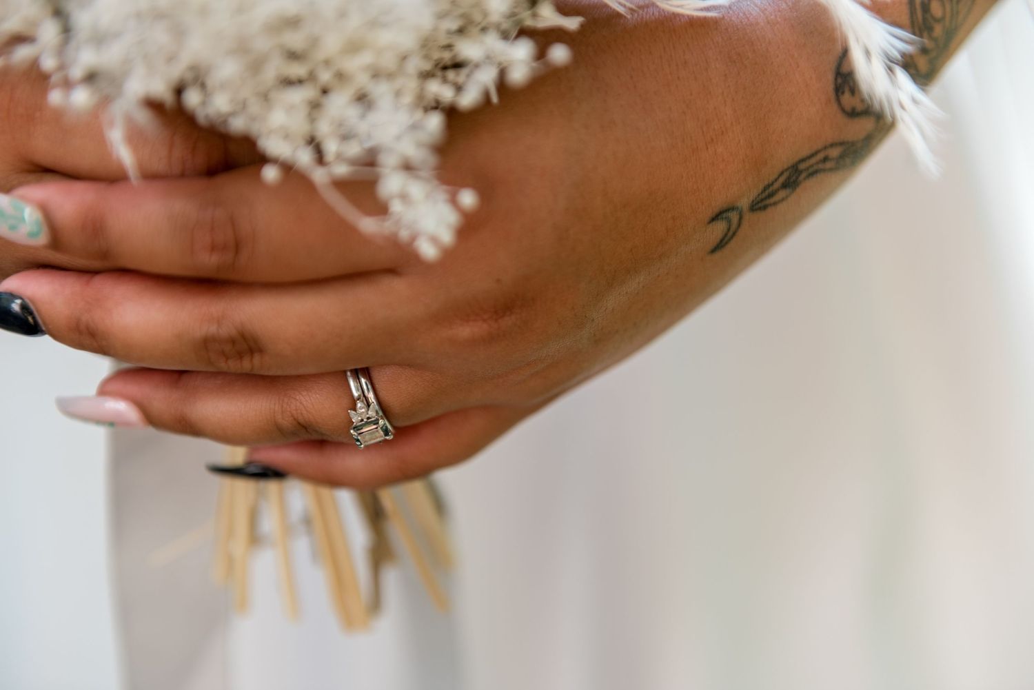 Close-up of a bride's hand with a diamond ring holding a white dried flower bouquet.