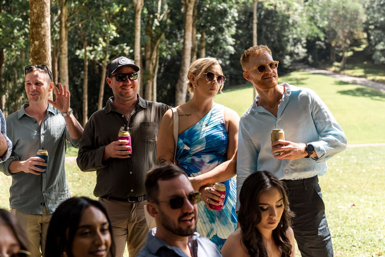 Wedding guests mingling outdoors in a lush green setting, holding drinks and enjoying the celebration.