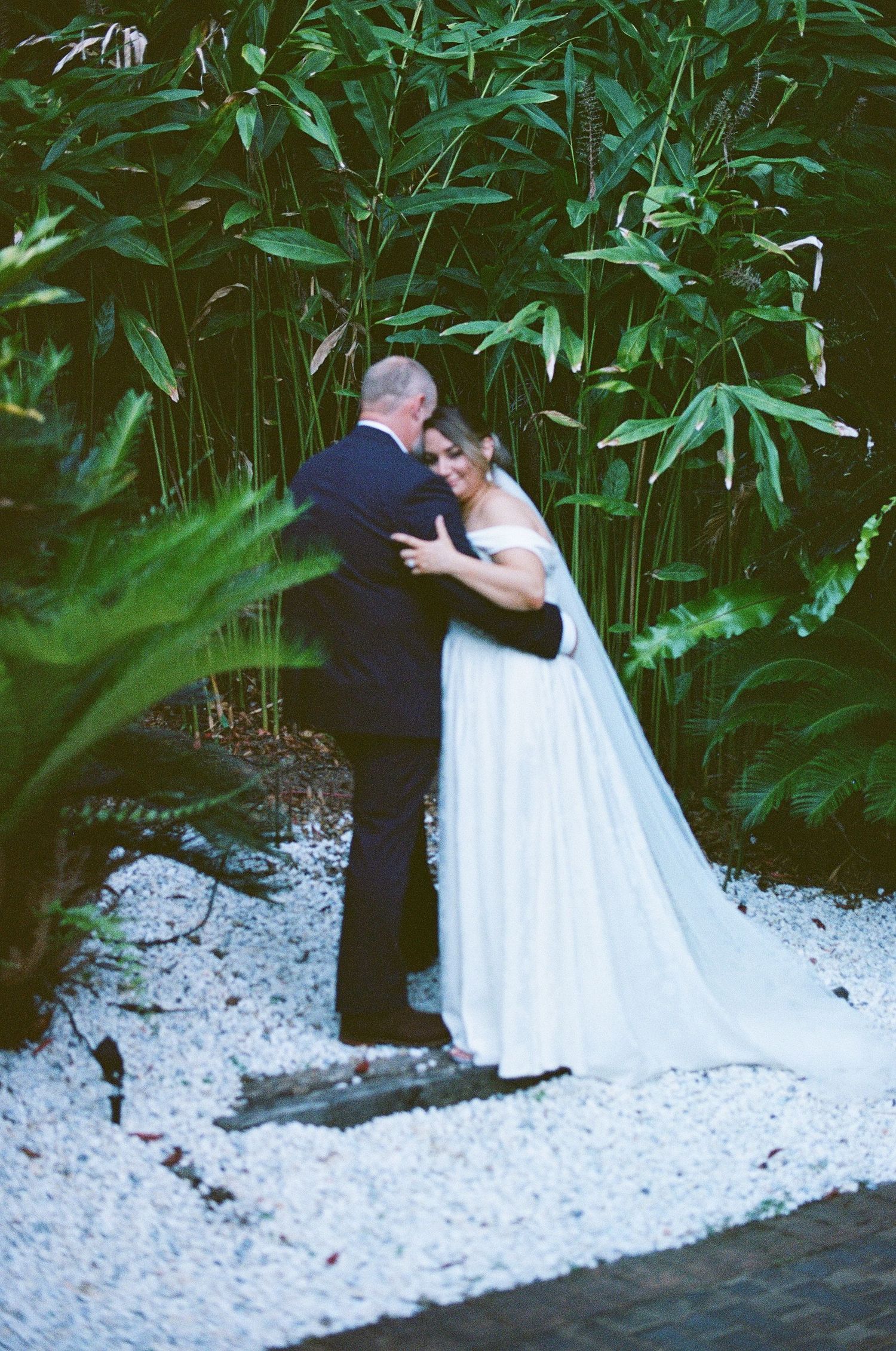 Bride and groom sharing tender embrace surrounded by lush tropical bamboo and green foliage at wedding.