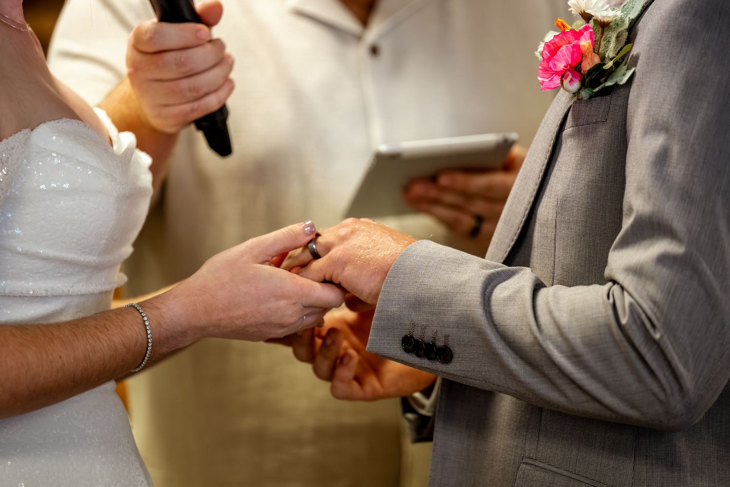 Close-up of couple holding hands during wedding ring exchange ceremony with officiant nearby.