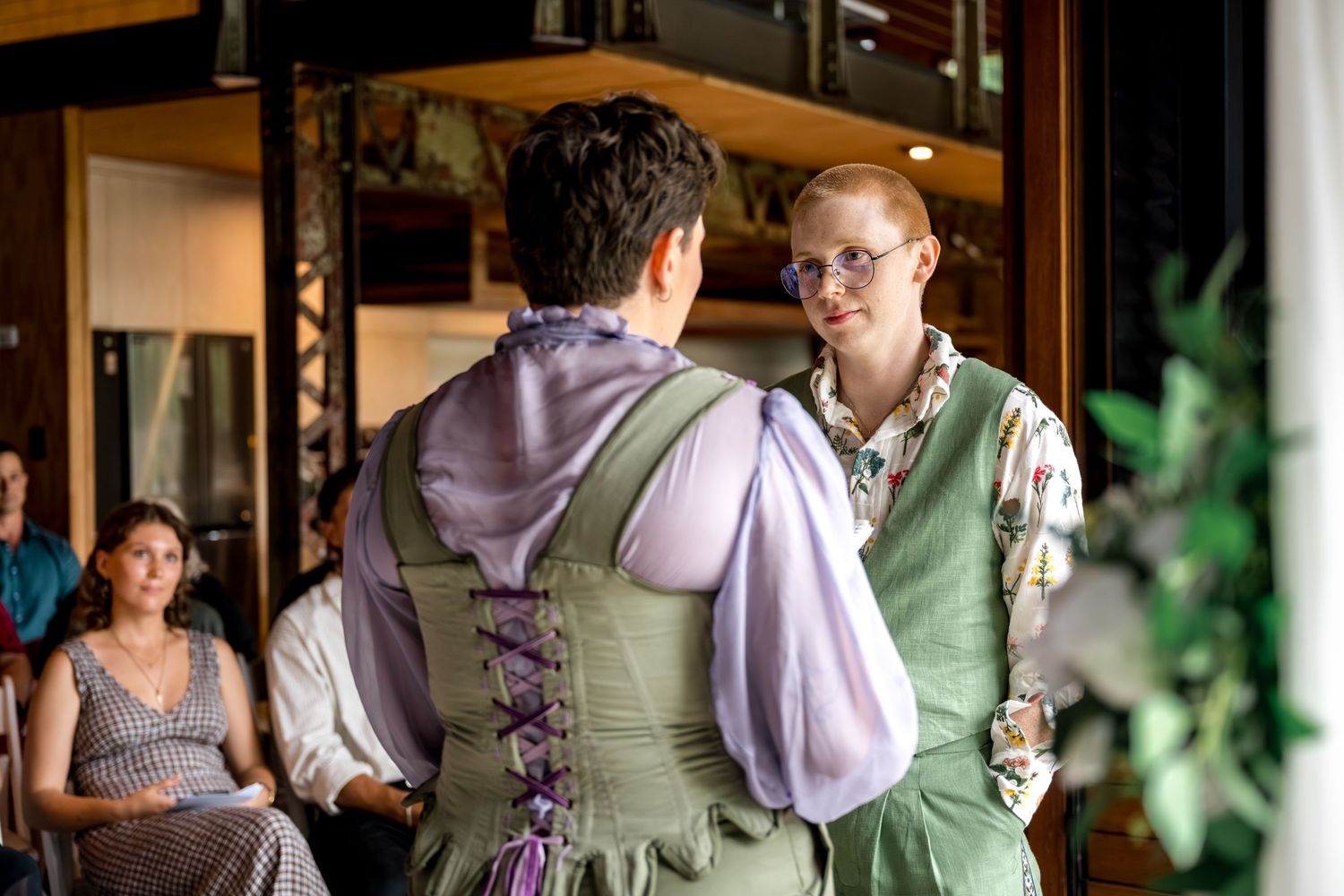Two brides face each other during emotional wedding vows in a rustic venue.