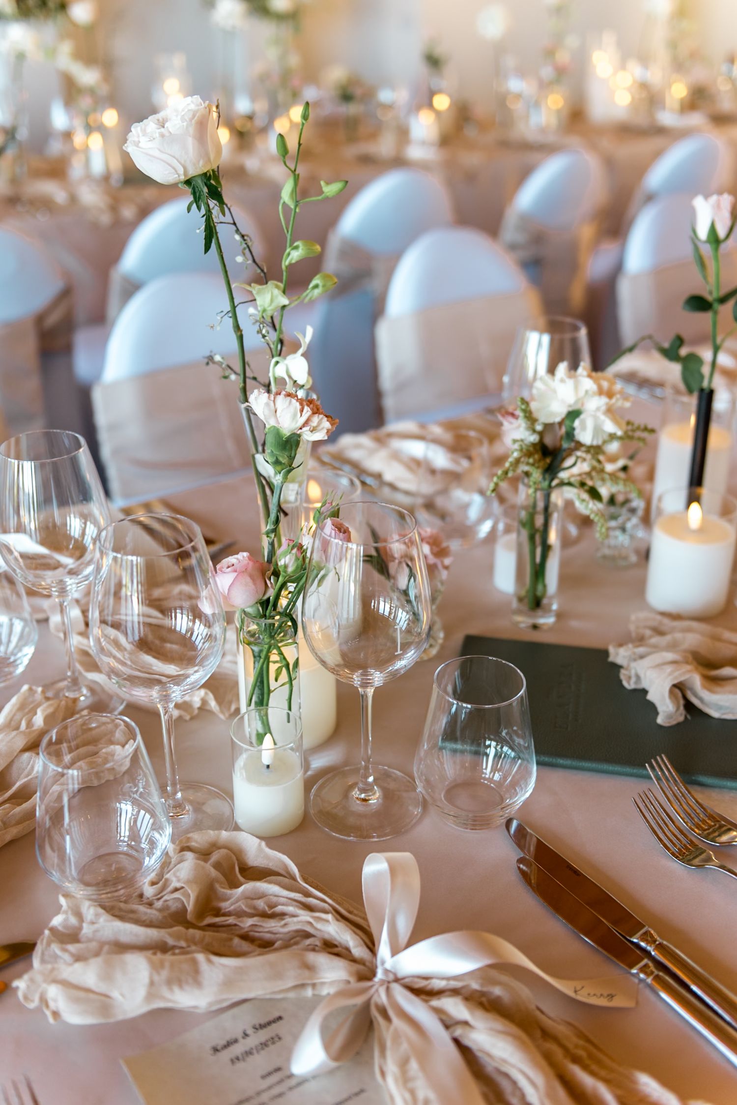 Elegant wedding reception table set with white roses, candles, crystal glasses, and satin ribbon napkins.