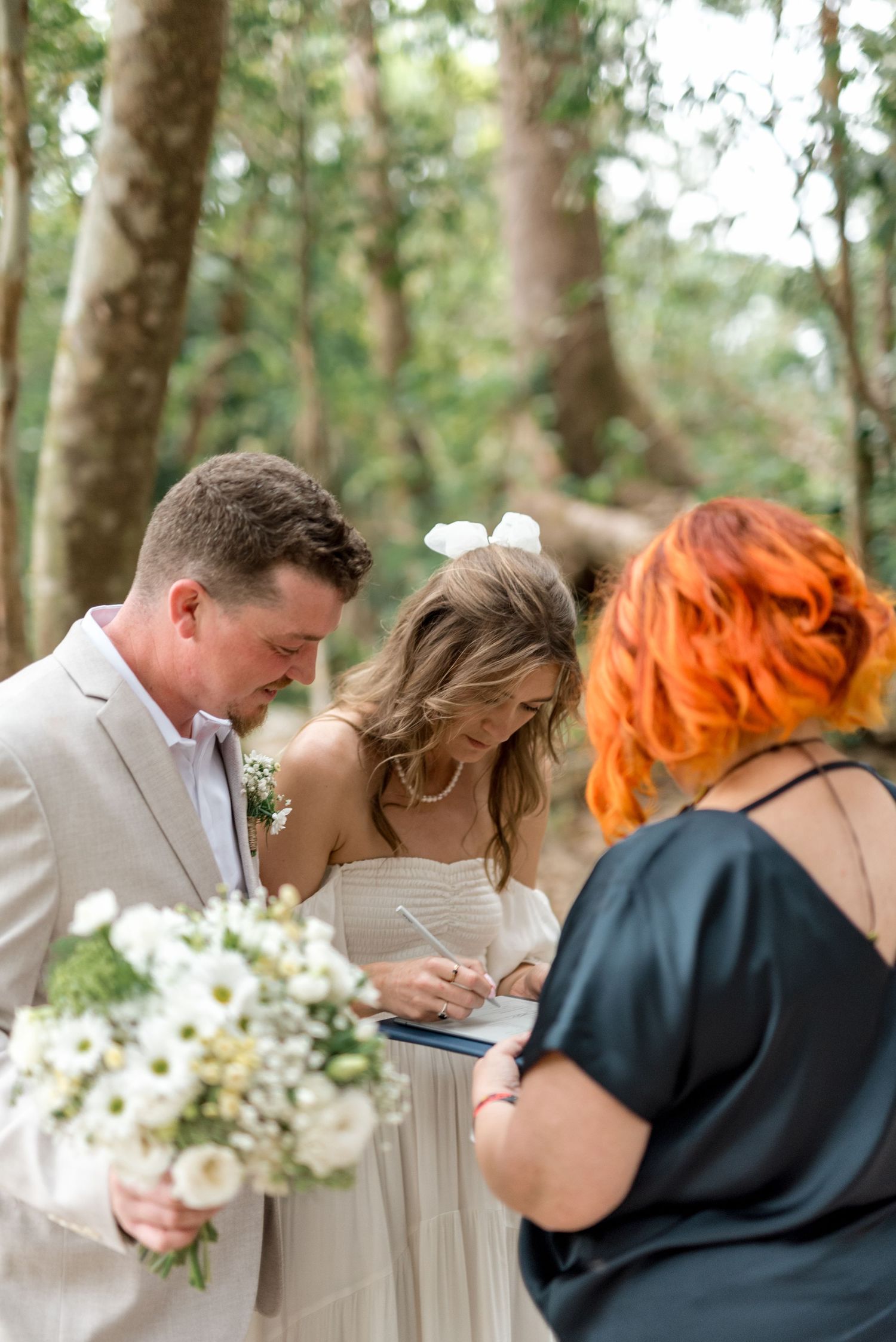 Bride signs wedding certificate with groom and officiant during intimate forest elopement ceremony.