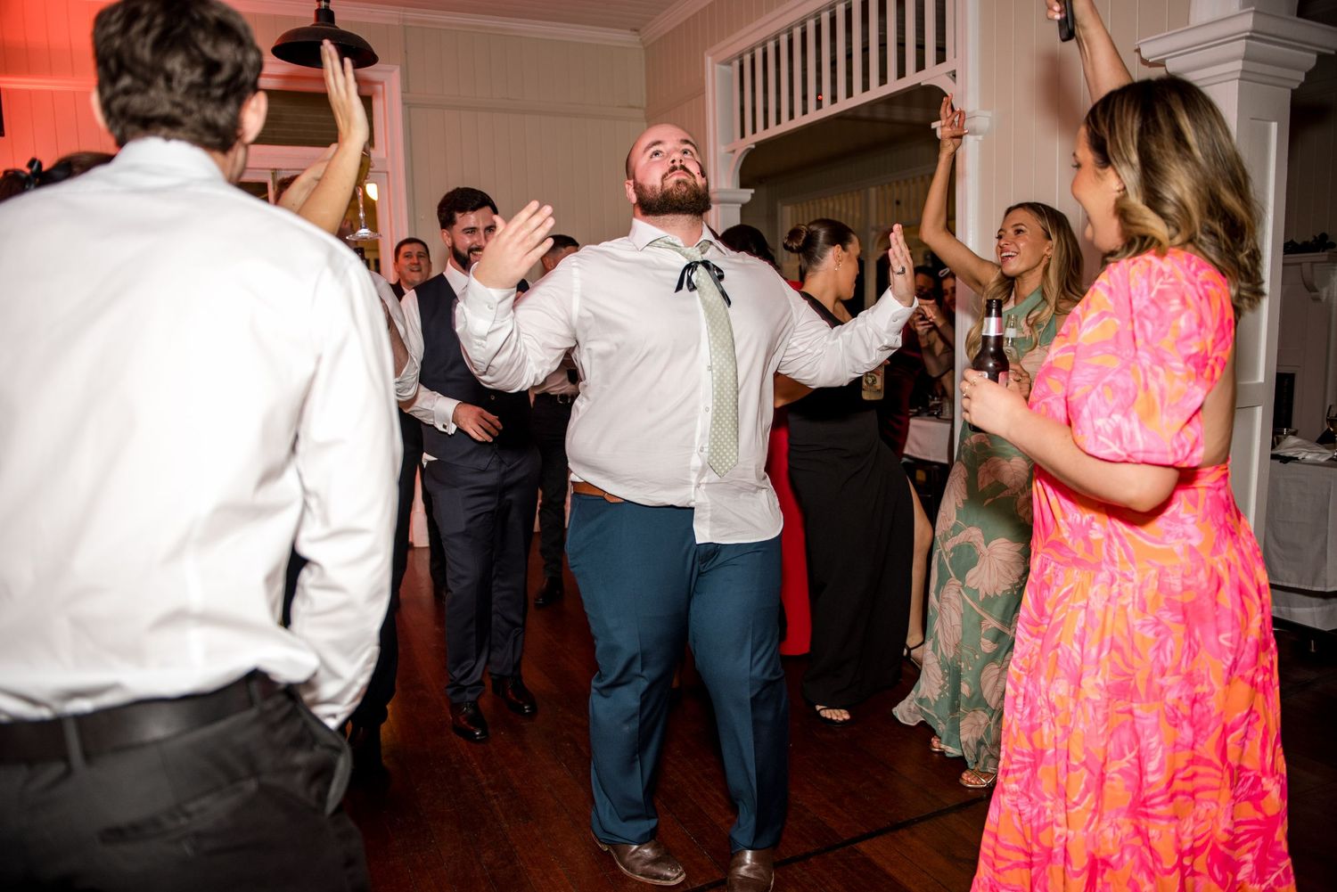 Wedding guest dancing enthusiastically with arms raised surrounded by celebrating guests at a lively reception.