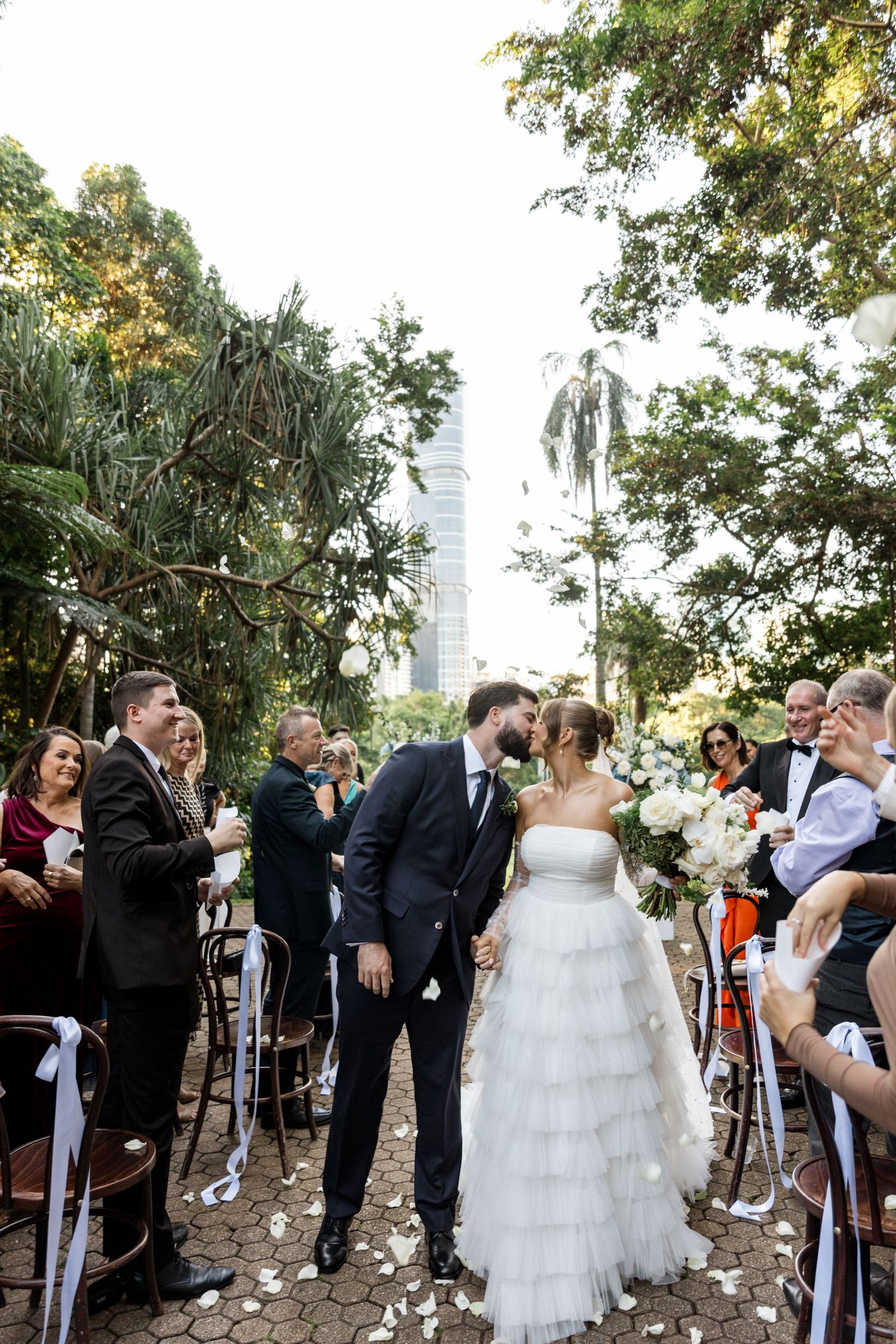 Bride and groom share a kiss while walking down the aisle at a lush outdoor garden wedding.