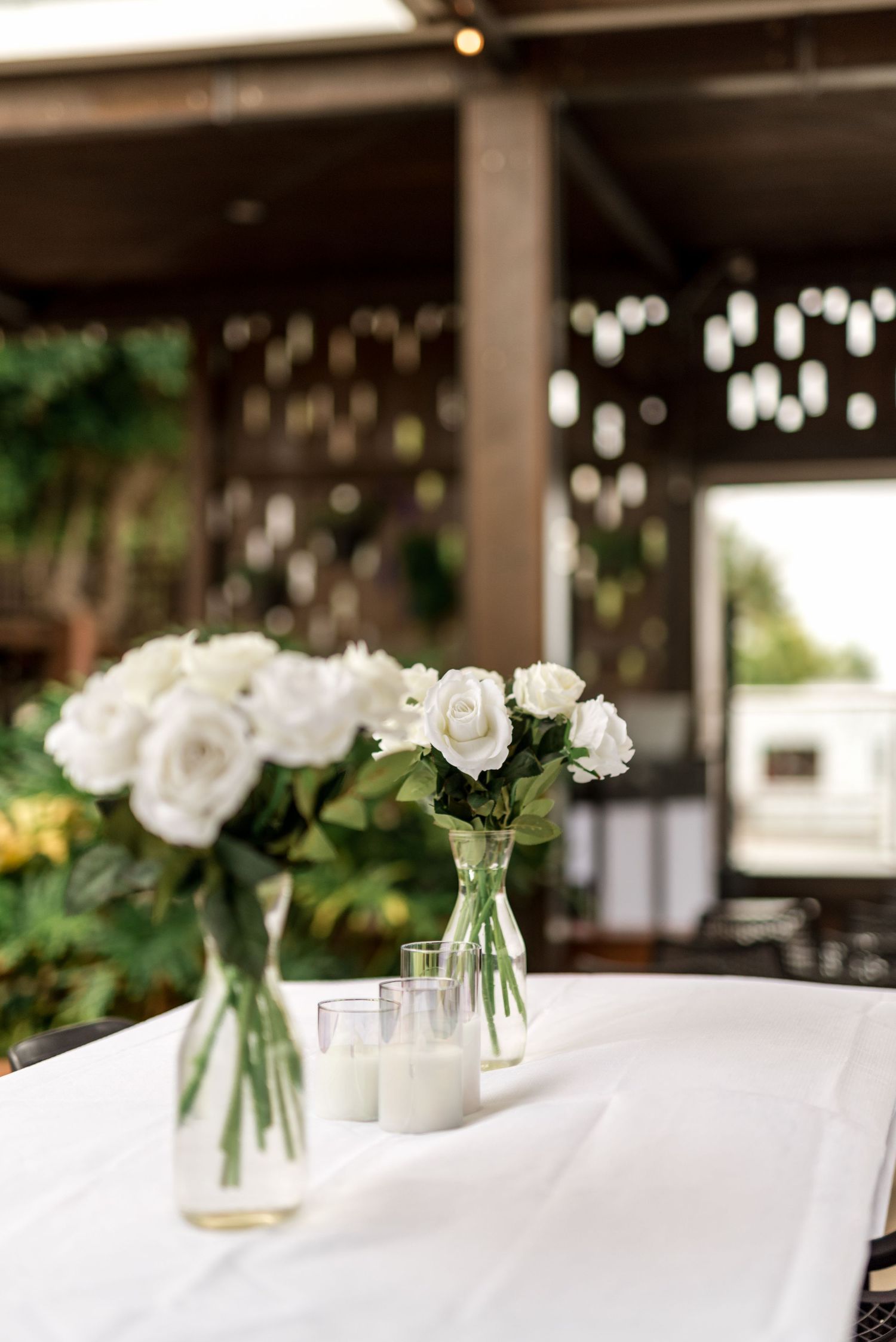 White rose centerpieces in glass vases with candles on white tablecloth at wedding reception.