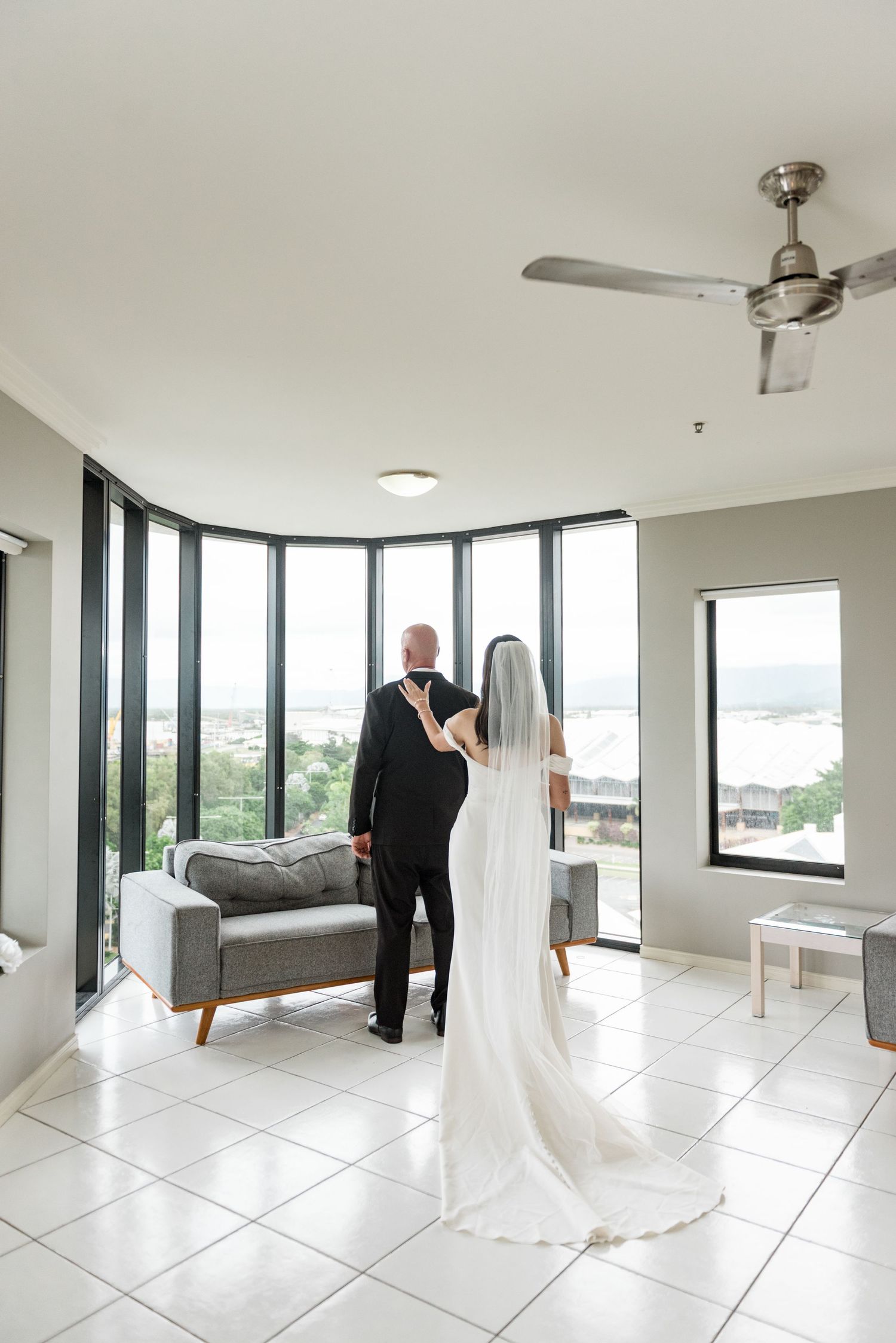 Bride and groom share a tender first look moment in a modern room with panoramic windows and city views.