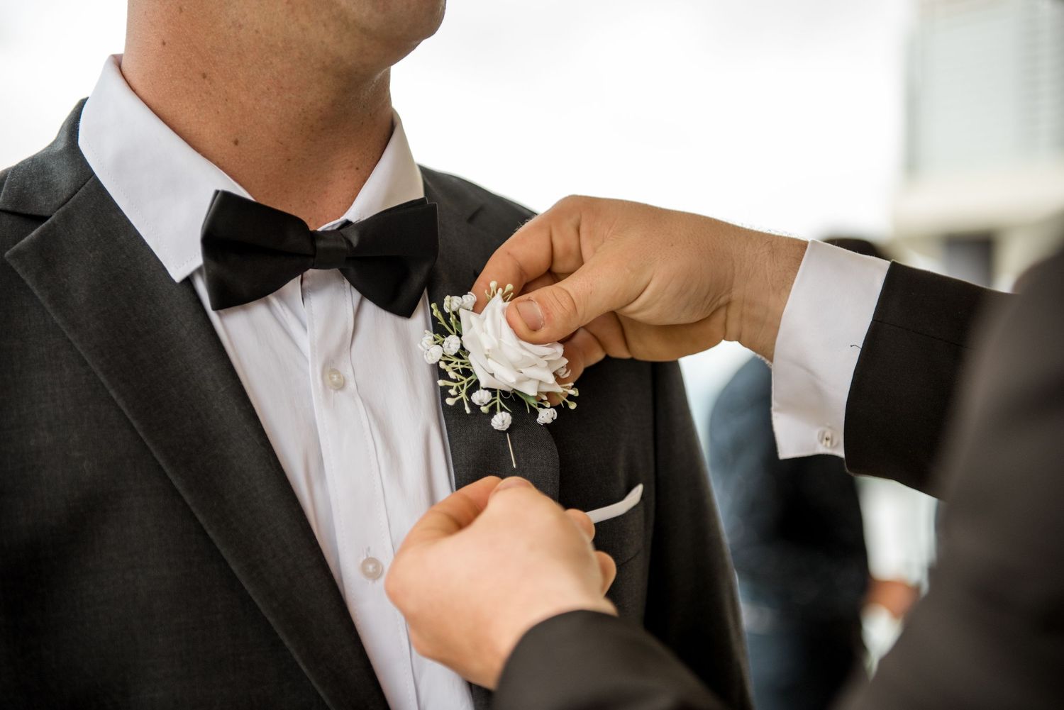 Close-up of hands pinning a white baby's breath boutonniere on a black tuxedo.