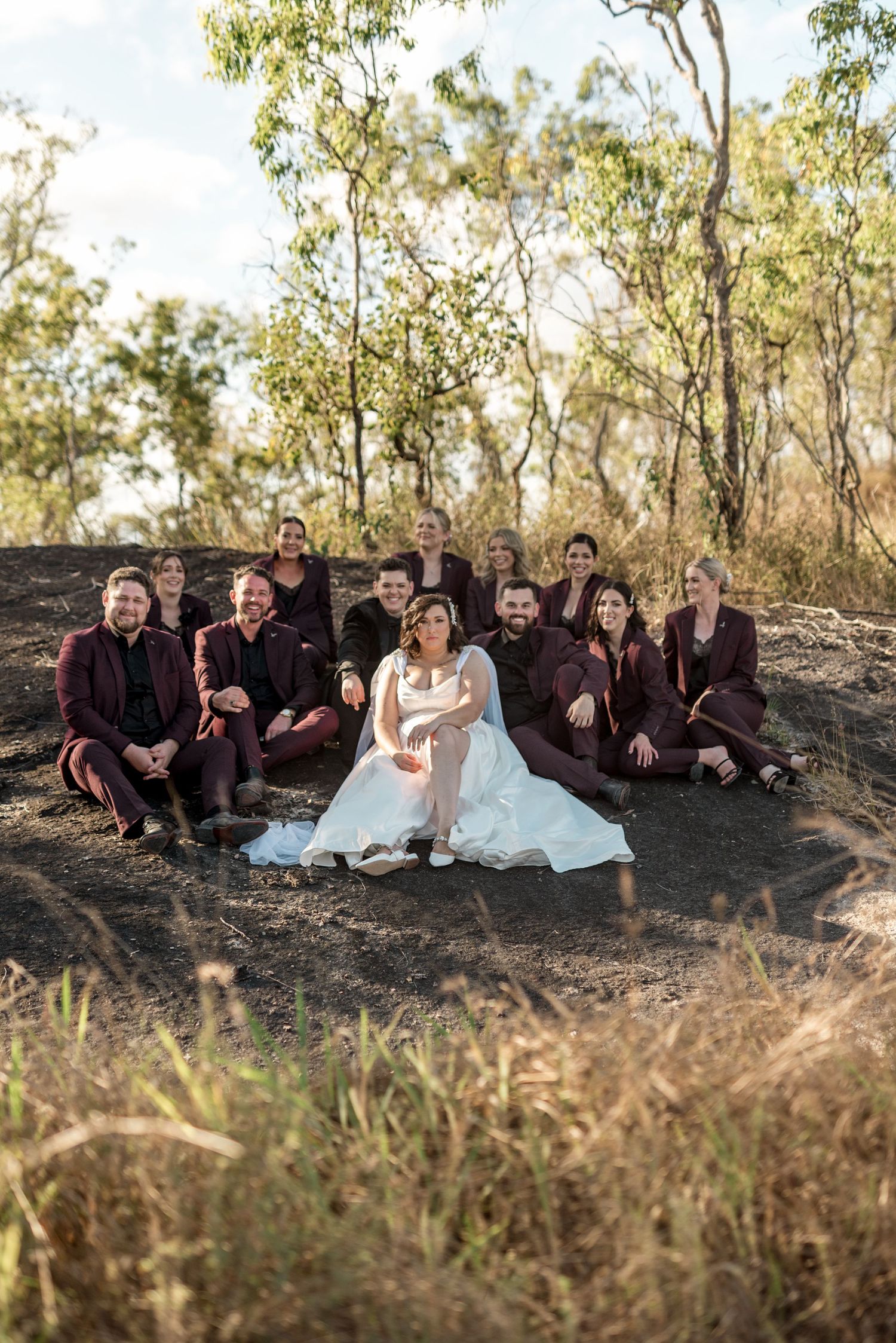 Wedding party in matching burgundy suits seated on a rocky hillside with Australian bushland backdrop surrounding the bride.