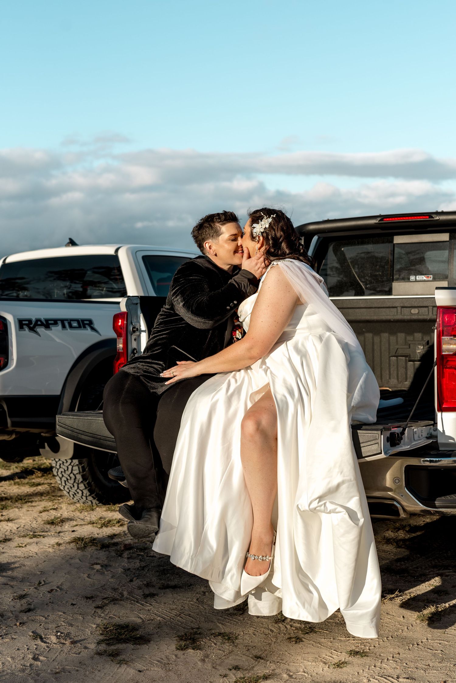 Bride and groom sharing a kiss while seated on a Ford Raptor truck tailgate.