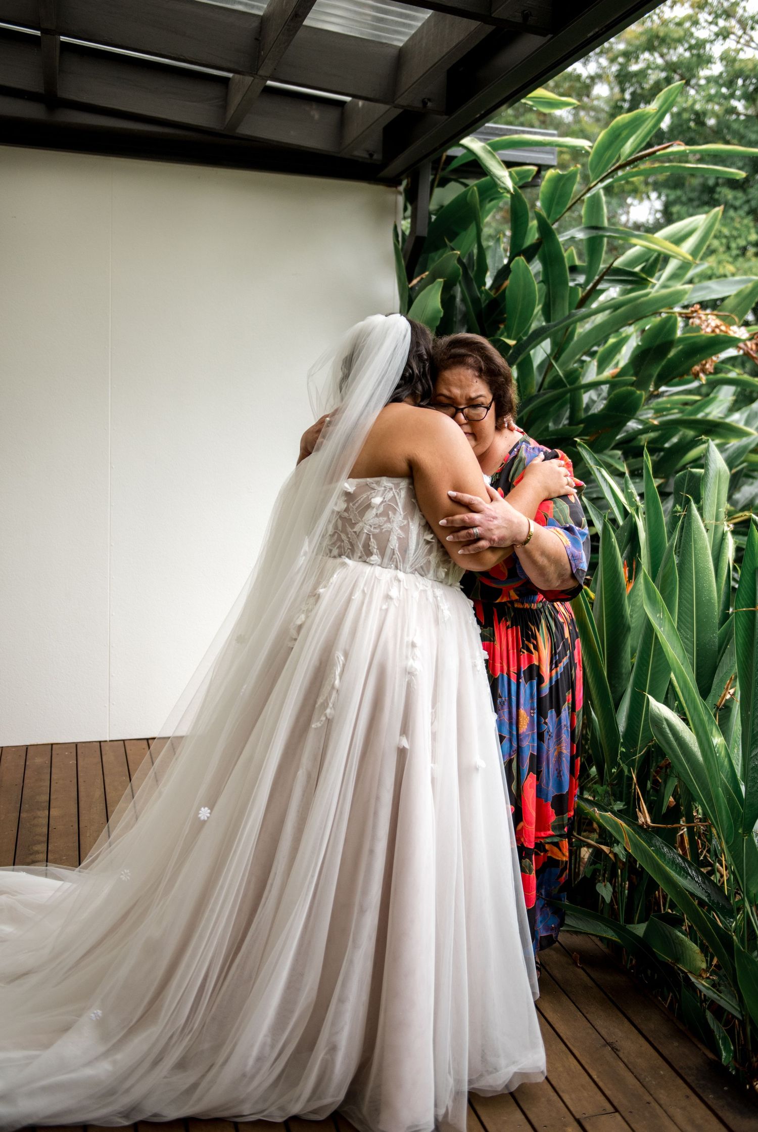 Bride in lace wedding gown with veil sharing an emotional hug with her mother before the ceremony.