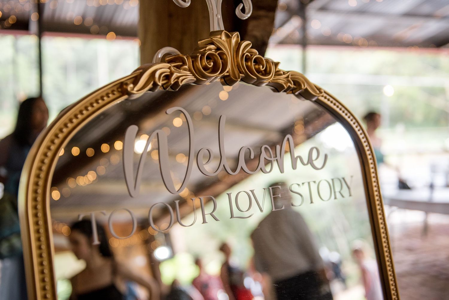 Ornate gold mirror with Welcome to Our Love Story calligraphy wedding sign.