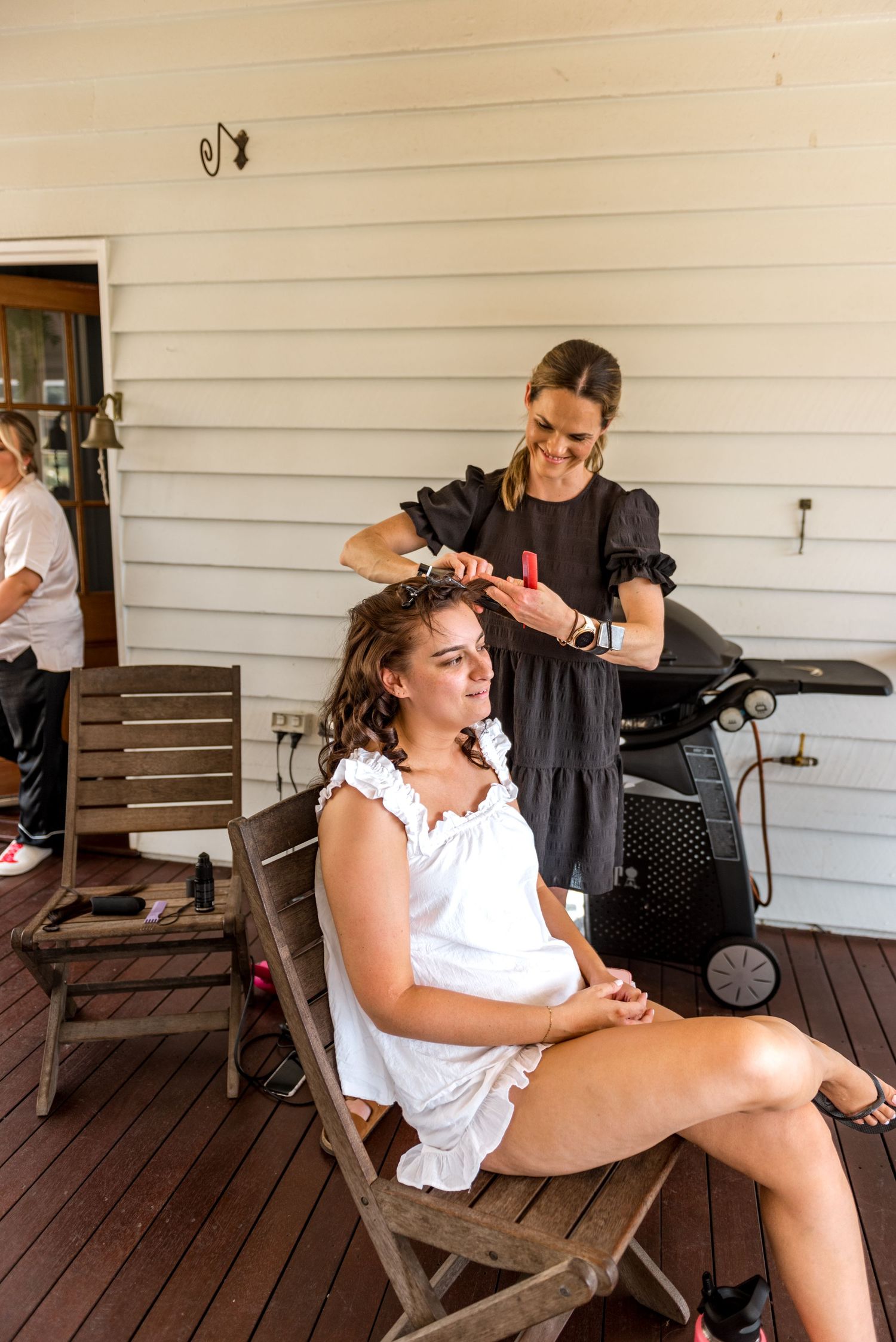 Hair stylist curling brides hair on a wooden porch using a curling iron outdoors.