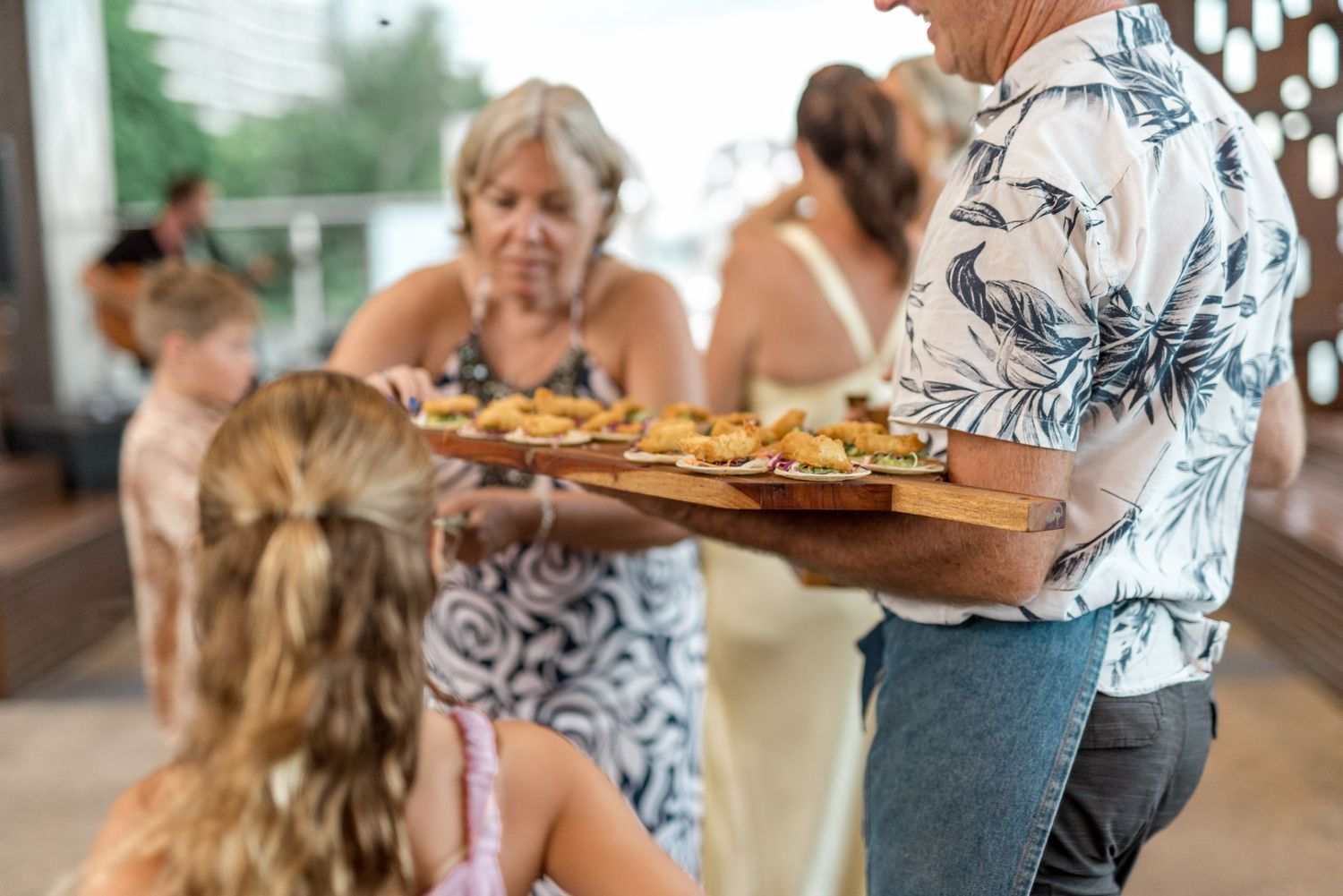 Guests being served appetizers on wooden board at elegant outdoor wedding reception event.