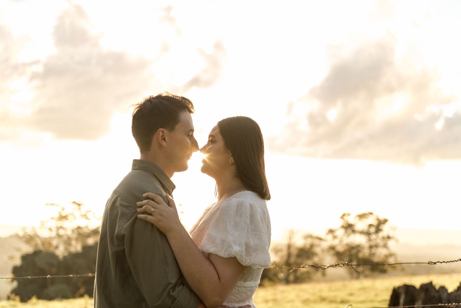 Couple about to kiss at golden hour with a scenic countryside backdrop.