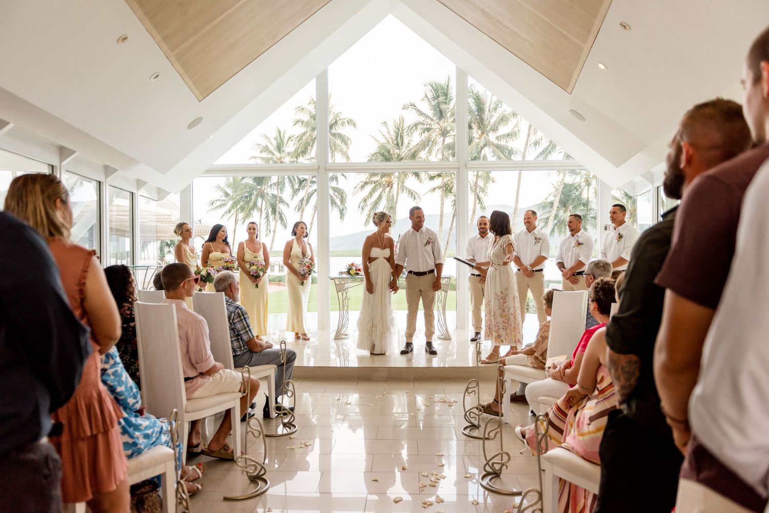 Wedding ceremony in a bright tropical chapel with guests seated and bridal party standing at the altar.