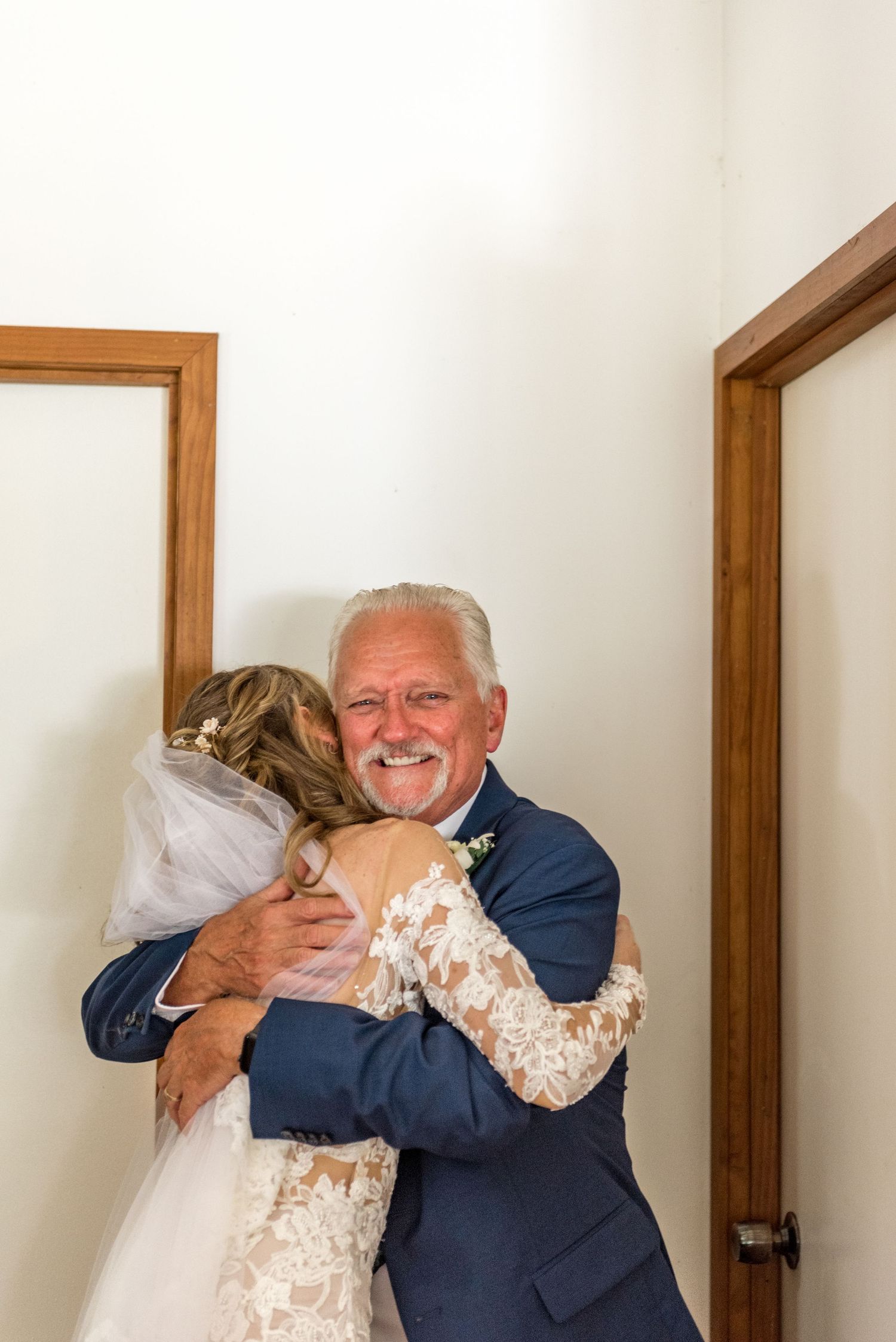 Emotional father of the bride hugging his daughter in her lace wedding gown before the ceremony.