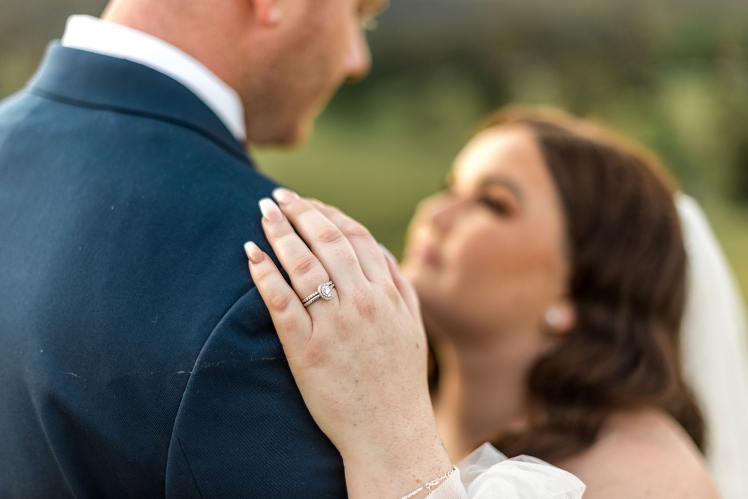Close-up of bride's diamond engagement ring as she places her hand on groom's navy suit jacket.