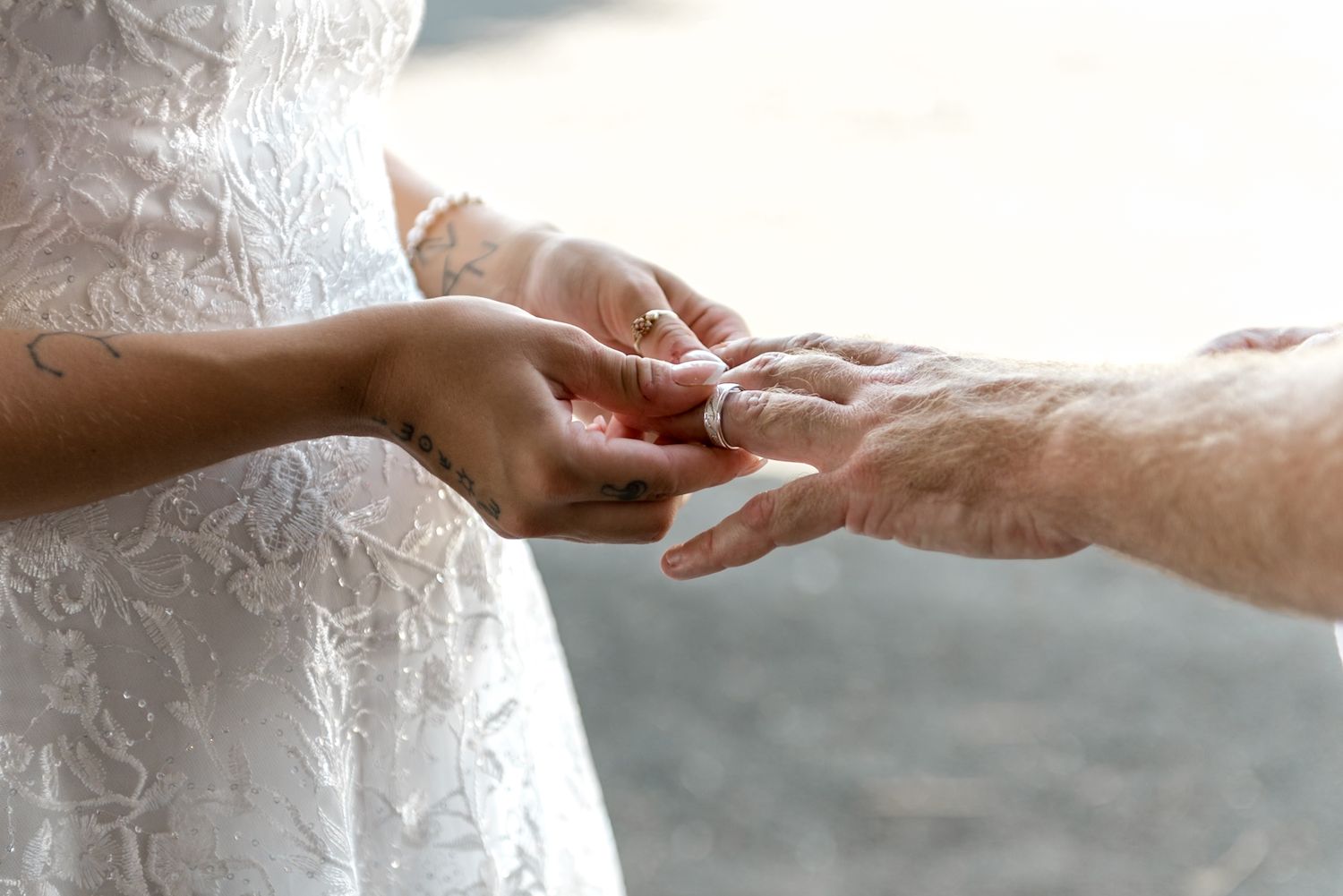 Bride and groom exchanging wedding rings during outdoor ceremony, close-up of hands.