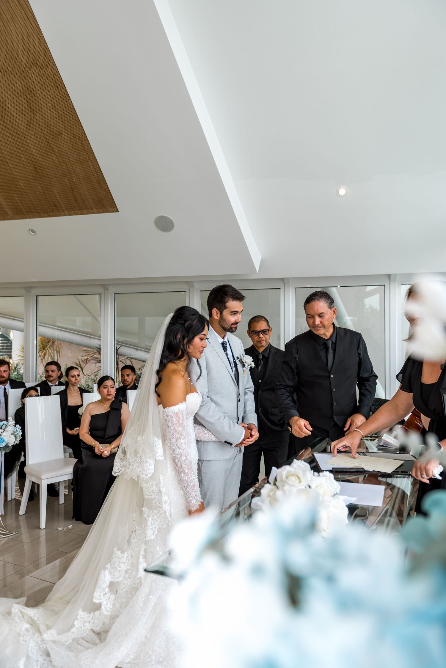 Bride and groom sign marriage certificate with officiant during elegant indoor beach wedding ceremony.