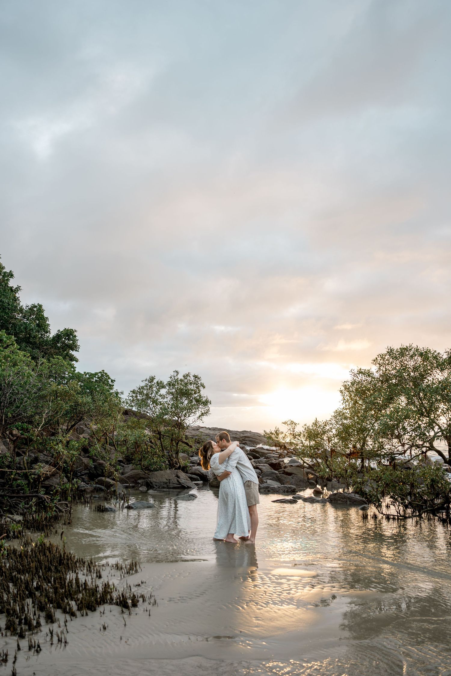 Couple sharing an intimate moment standing in shallow water at a stunning tropical sunset beach at Four Mile Beach, Port Douglas.