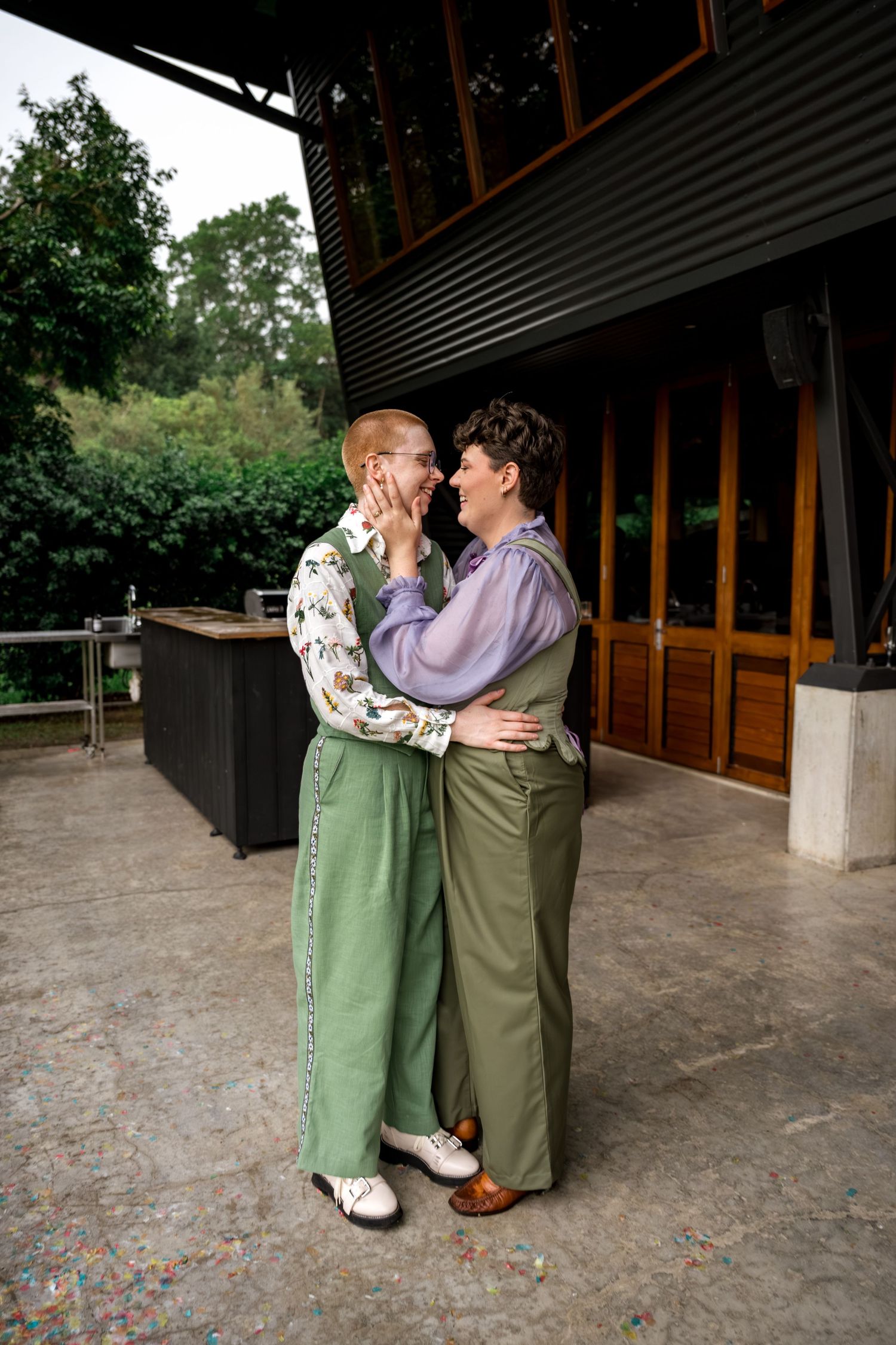 Two people in green outfits embracing and smiling at each other on an outdoor patio.