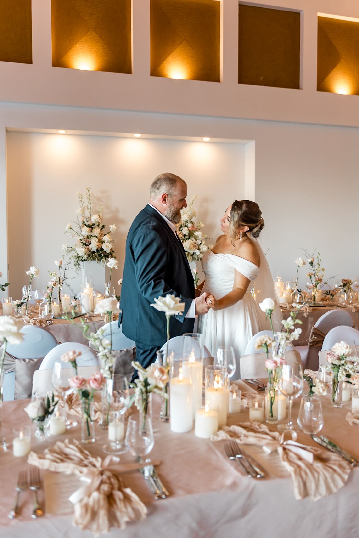 Bride and groom hold hands and gaze at each other at their romantic candlelit wedding reception.