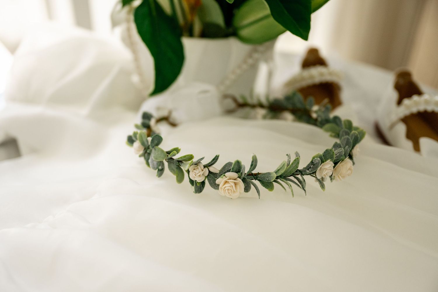Delicate floral crown with white roses and eucalyptus leaves on white fabric background.