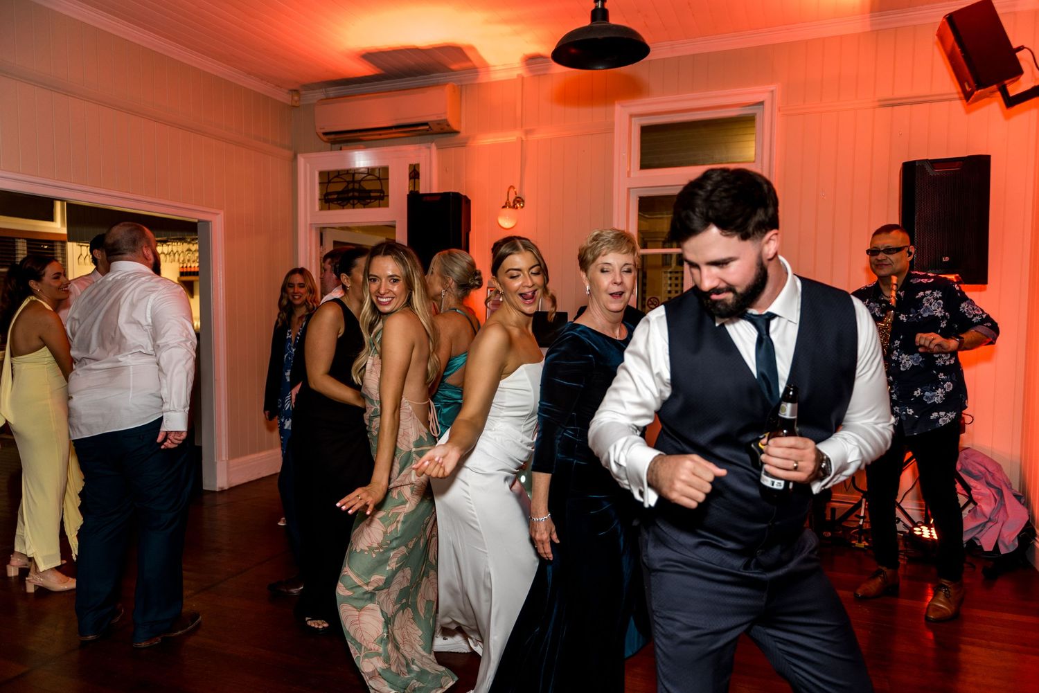 Bride in white gown dancing with groom in vest at a lively wedding reception.