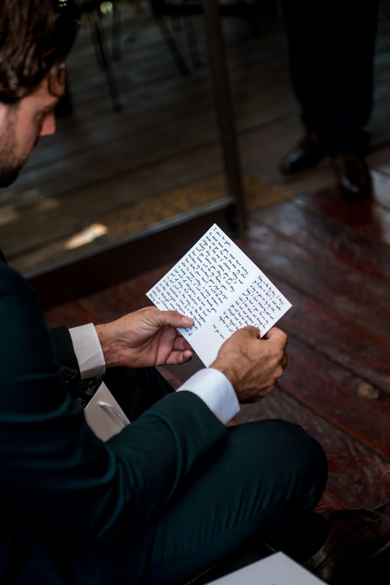 Groom in teal suit reading handwritten letter before wedding ceremony.