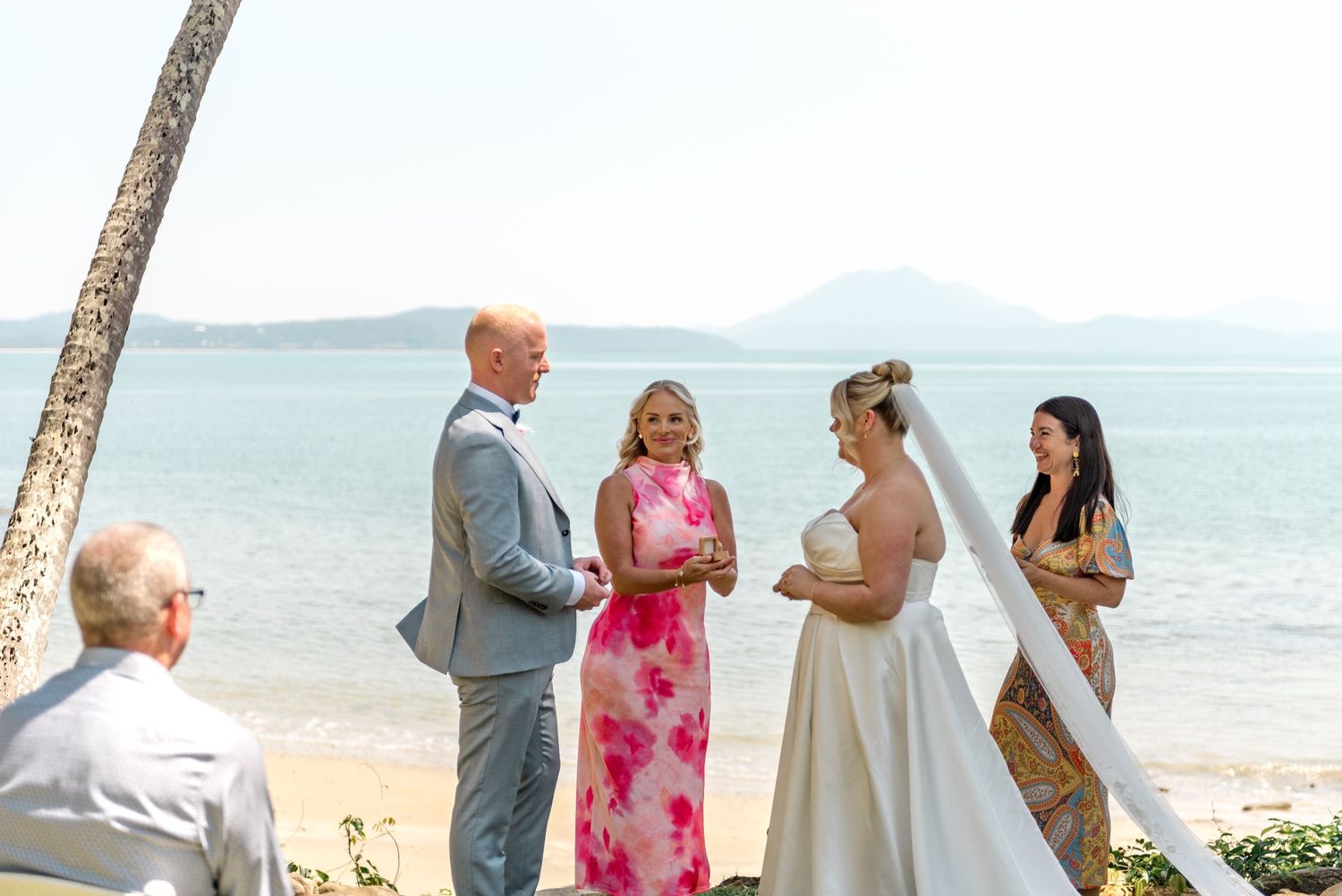 Wedding celebrant in pink dress officiates intimate beach ceremony with bride and groom.