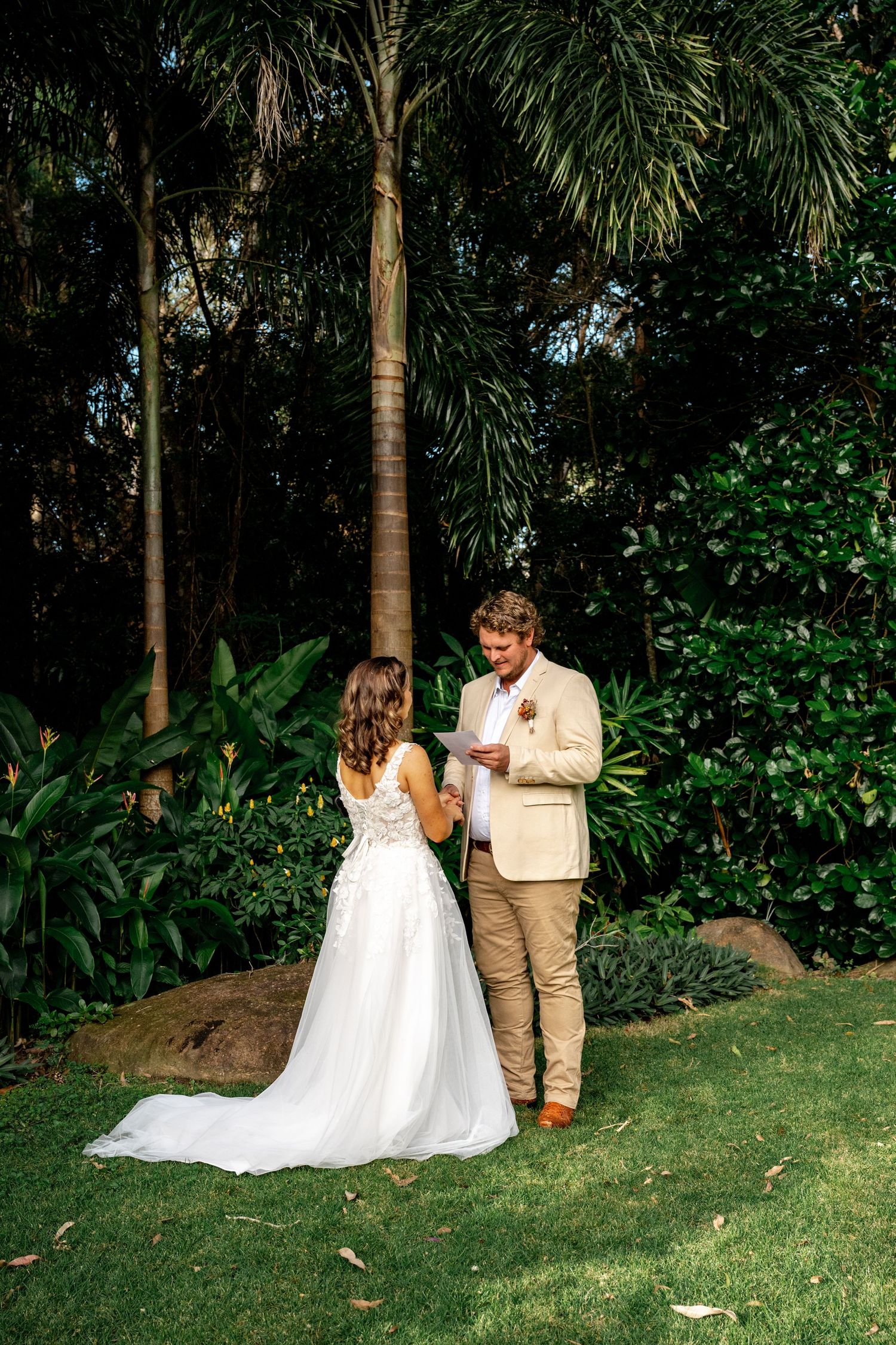 Bride and groom exchange vows in lush tropical garden setting during intimate outdoor wedding ceremony.