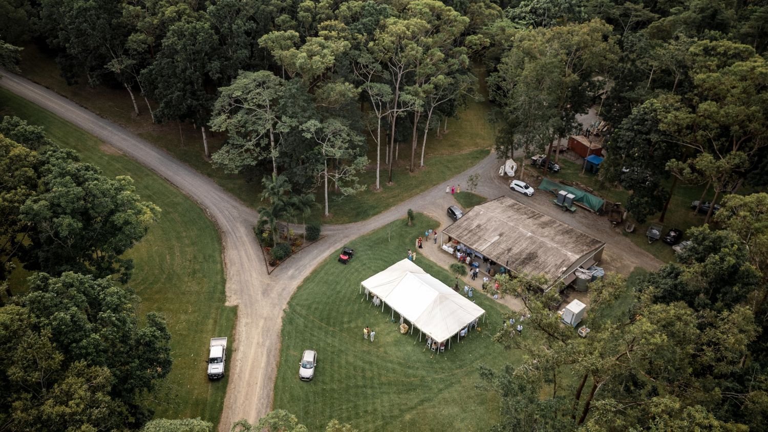 Aerial view of a wedding venue with white marquee tent nestled among lush green forest and driveway.