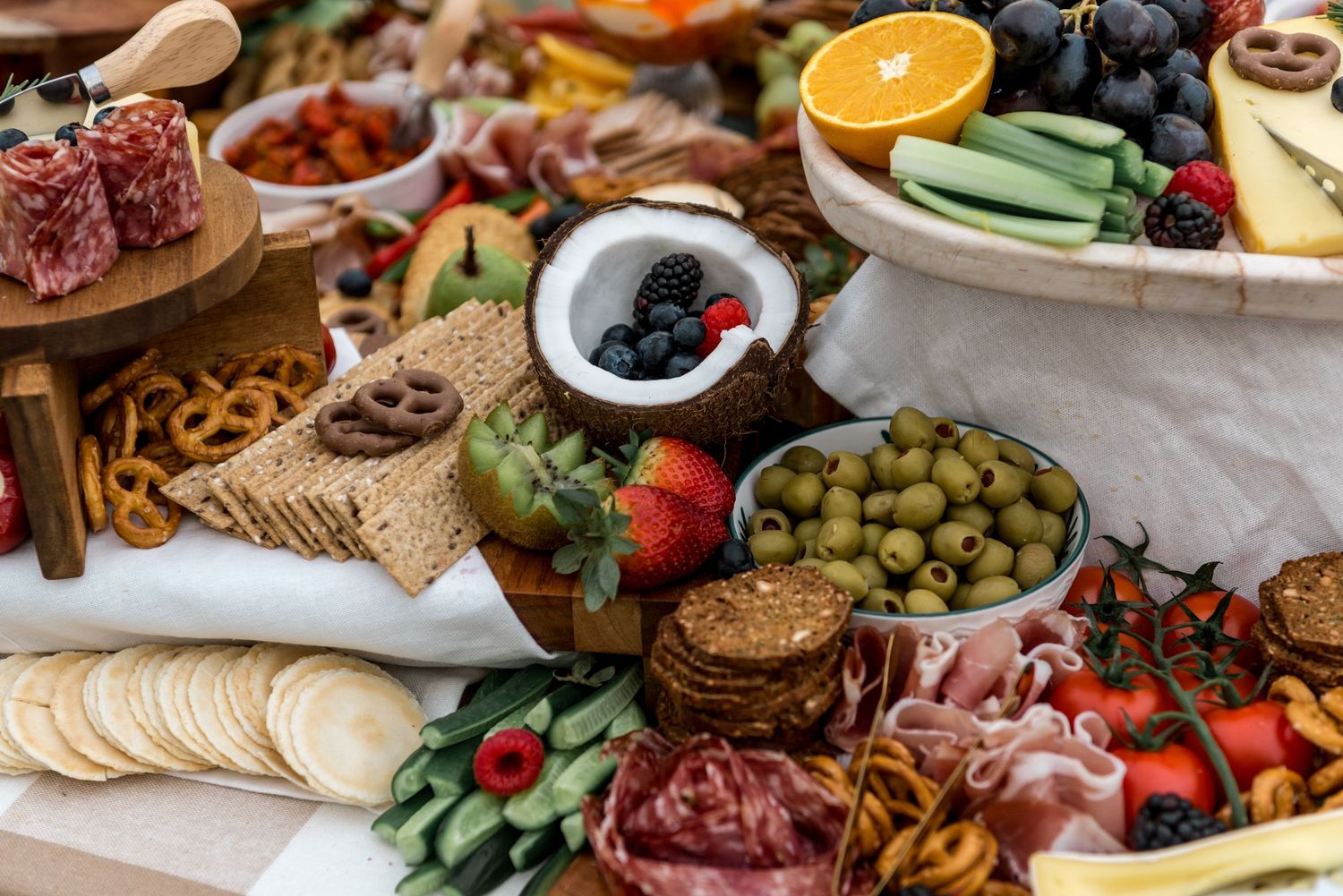 Stunning grazing table spread featuring fruits, meats, olives, crackers, and a coconut berry bowl.