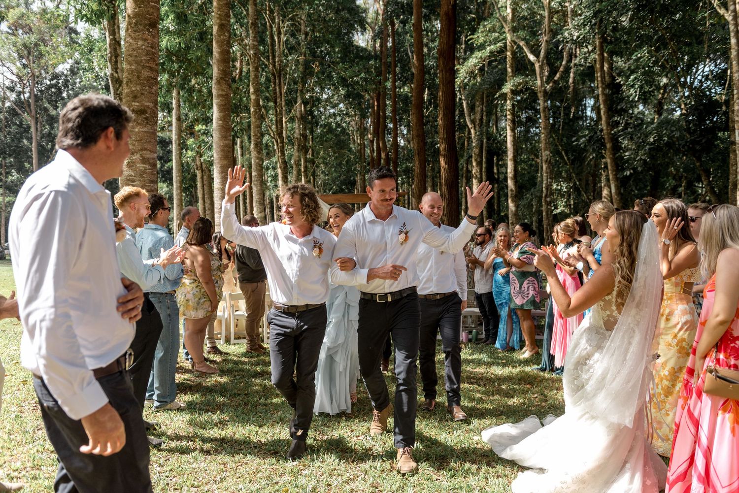 Groom and groomsmen celebrating joyfully at an outdoor wedding ceremony in a lush forest setting.