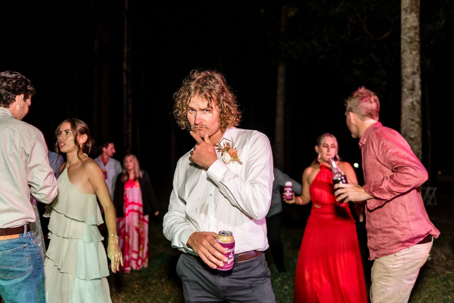 Curly-haired man in white shirt mingling with guests at outdoor nighttime wedding party.