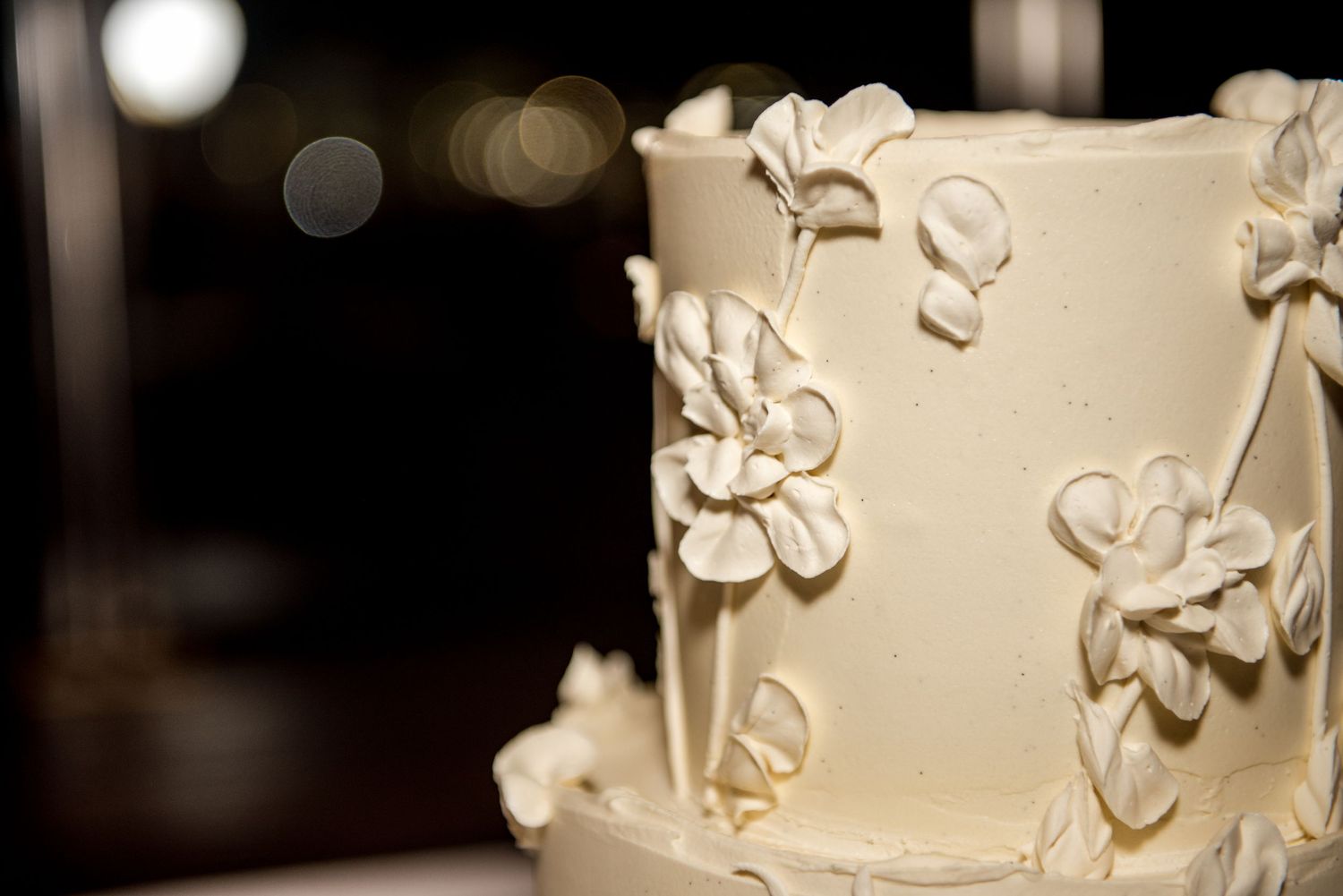 Close-up of an elegant two-tier white wedding cake adorned with delicate handcrafted sugar flowers.