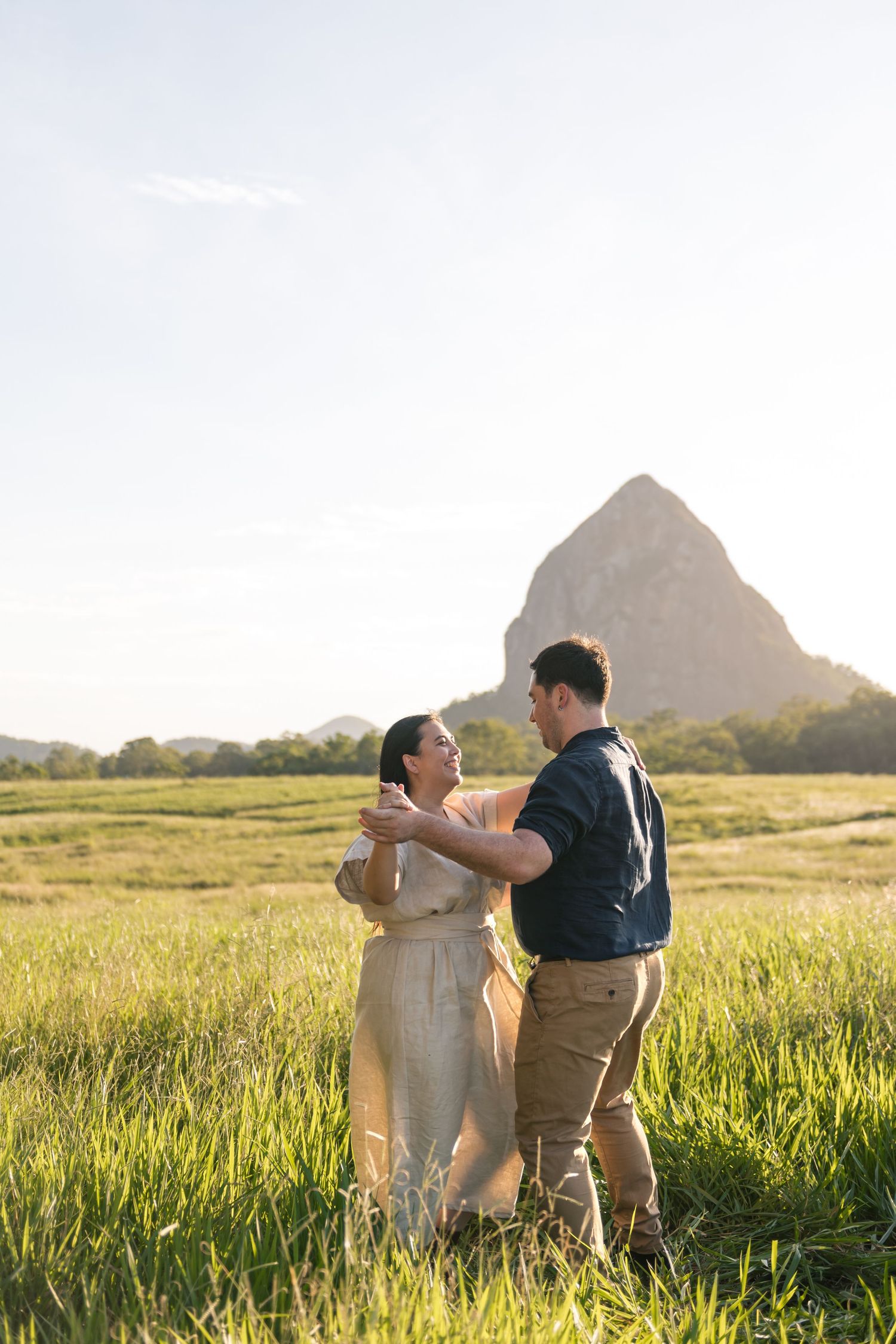 Couple dancing together in a bright green field with a dramatic rocky mountain peak in the background.