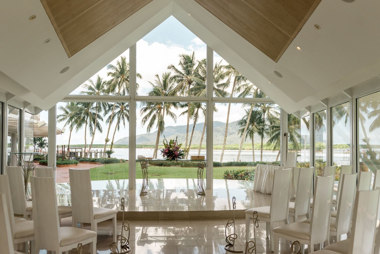Stunning beach wedding venue interior with floor-to-ceiling windows overlooking tropical palm trees.