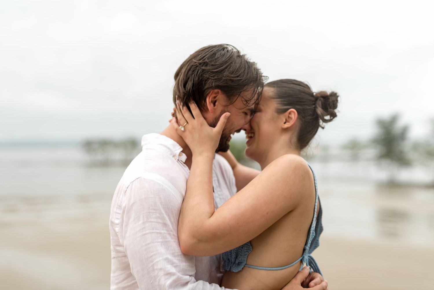 Close-up of a couple sharing a tender kiss on a cloudy tropical beach.