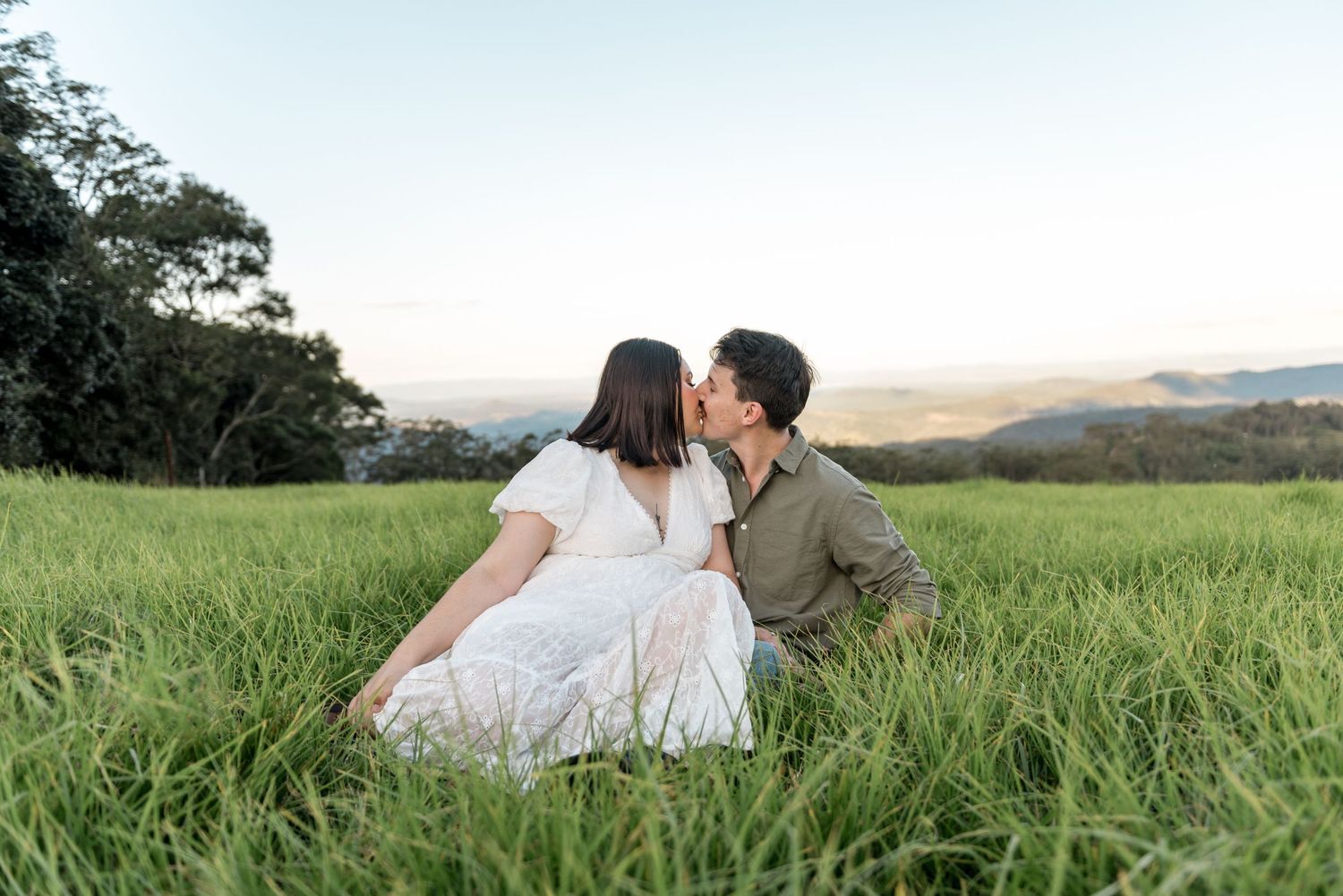 Couple sharing a sweet kiss while sitting together in tall green grass.