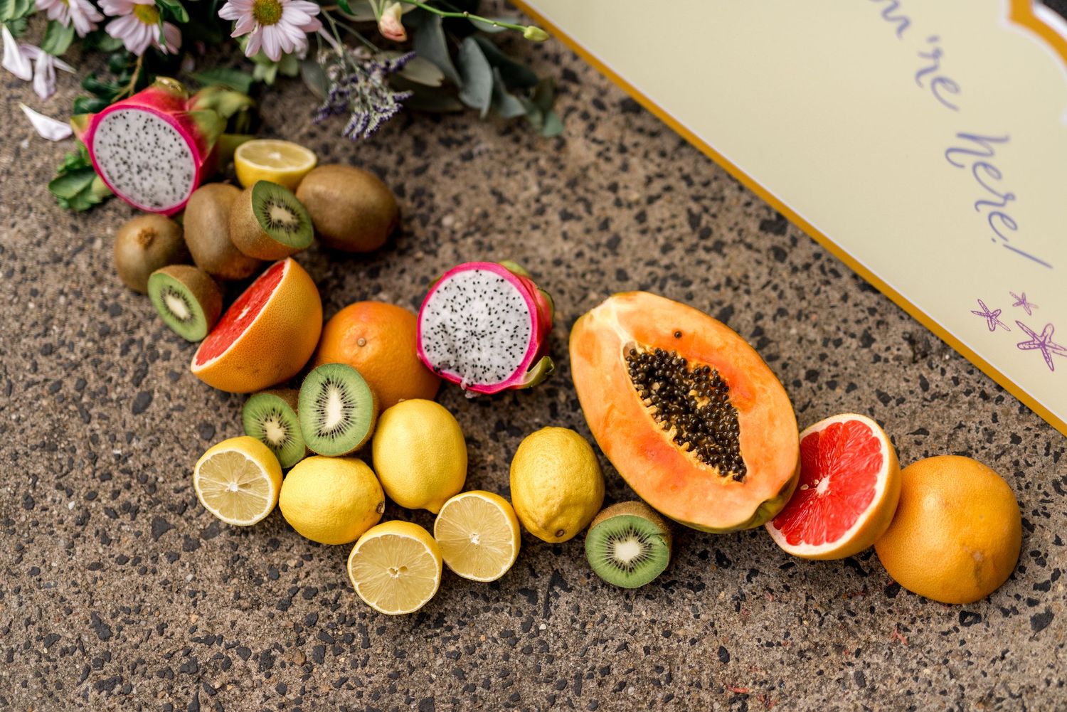 Colorful assortment of tropical fruits including papaya, dragon fruit, kiwi, and citrus on granite surface.