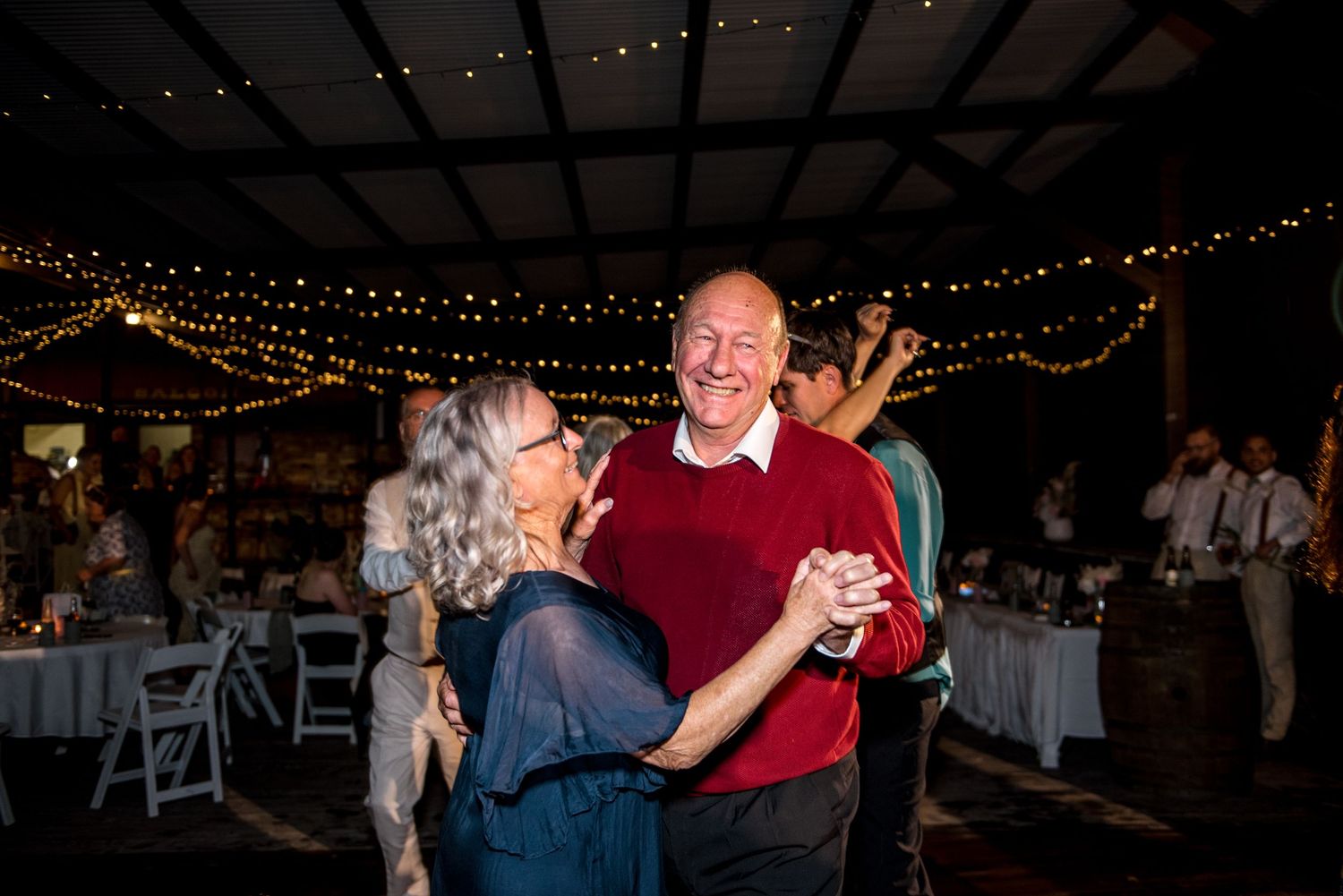 Older couple smiling and dancing together joyfully at an evening wedding reception.