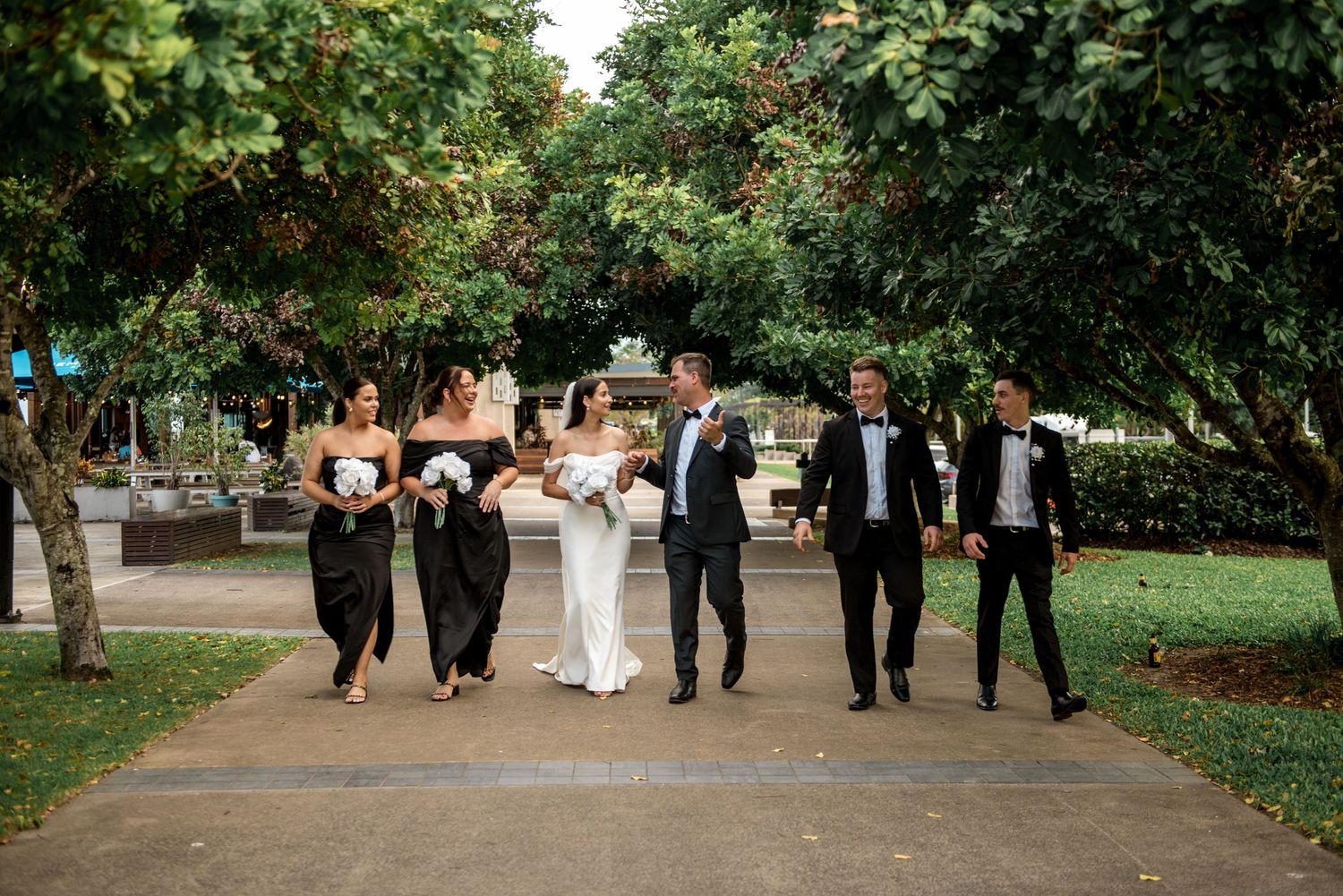 Elegant wedding party in black and white attire walking through a park.
