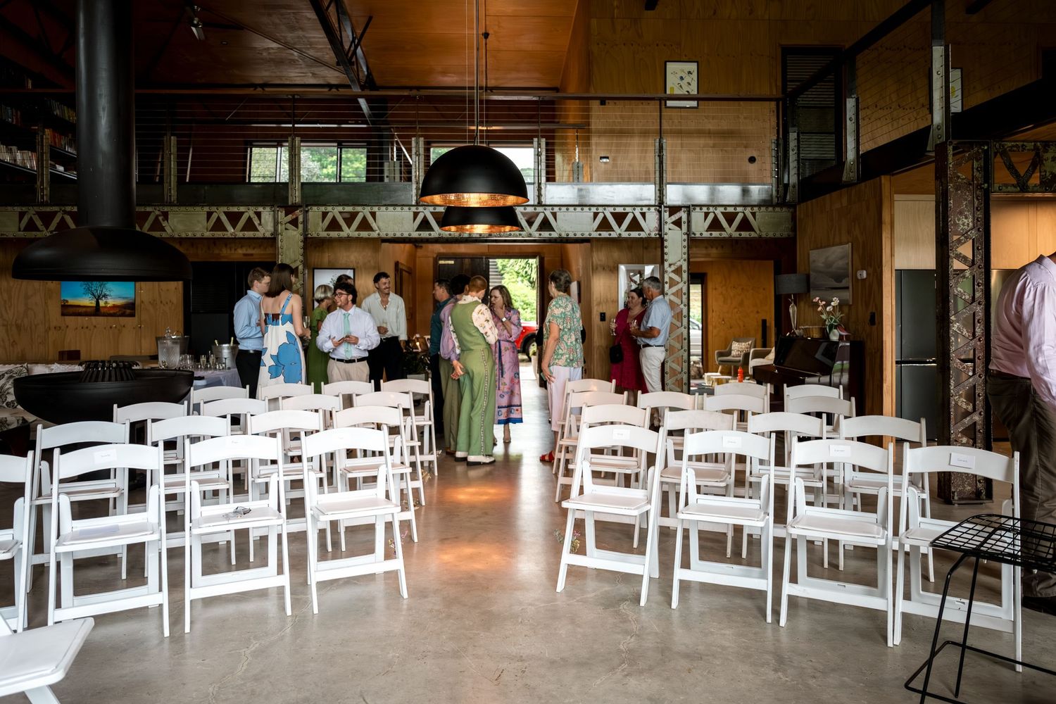 Rustic wooden wedding venue interior with white folding chairs and guests mingling before ceremony.