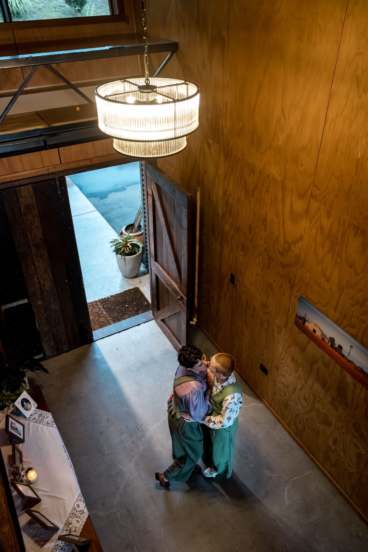 Aerial view of two women dancing beneath a chandelier in a rustic wooden venue.