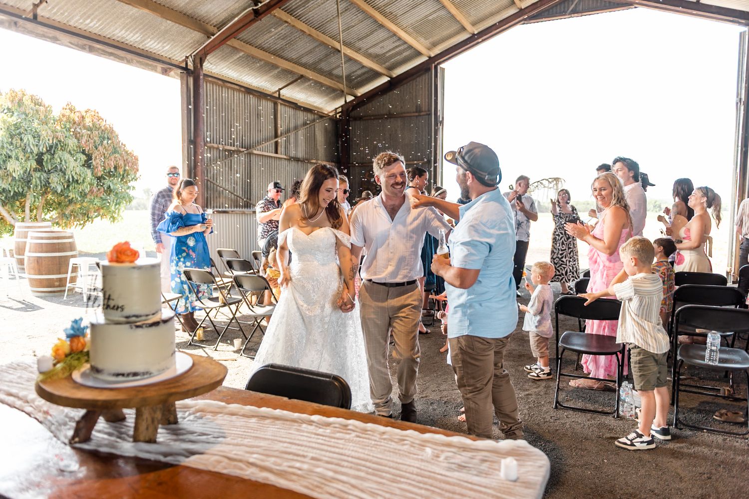 Bride and groom share a joyful moment near wedding cake in a barn venue.