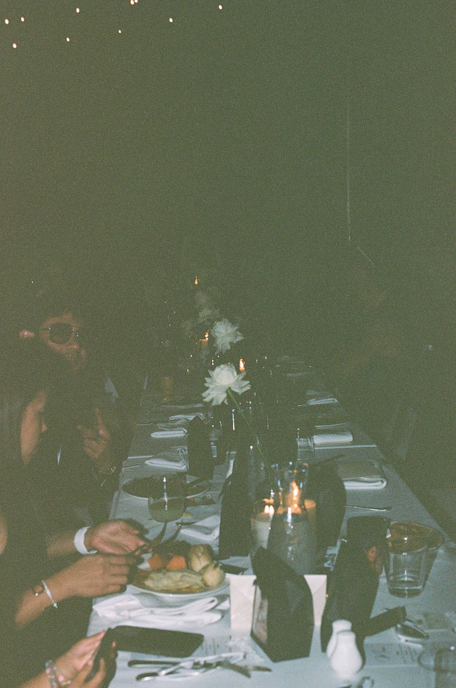 Wedding guests dining at candlelit outdoor reception table at night.
