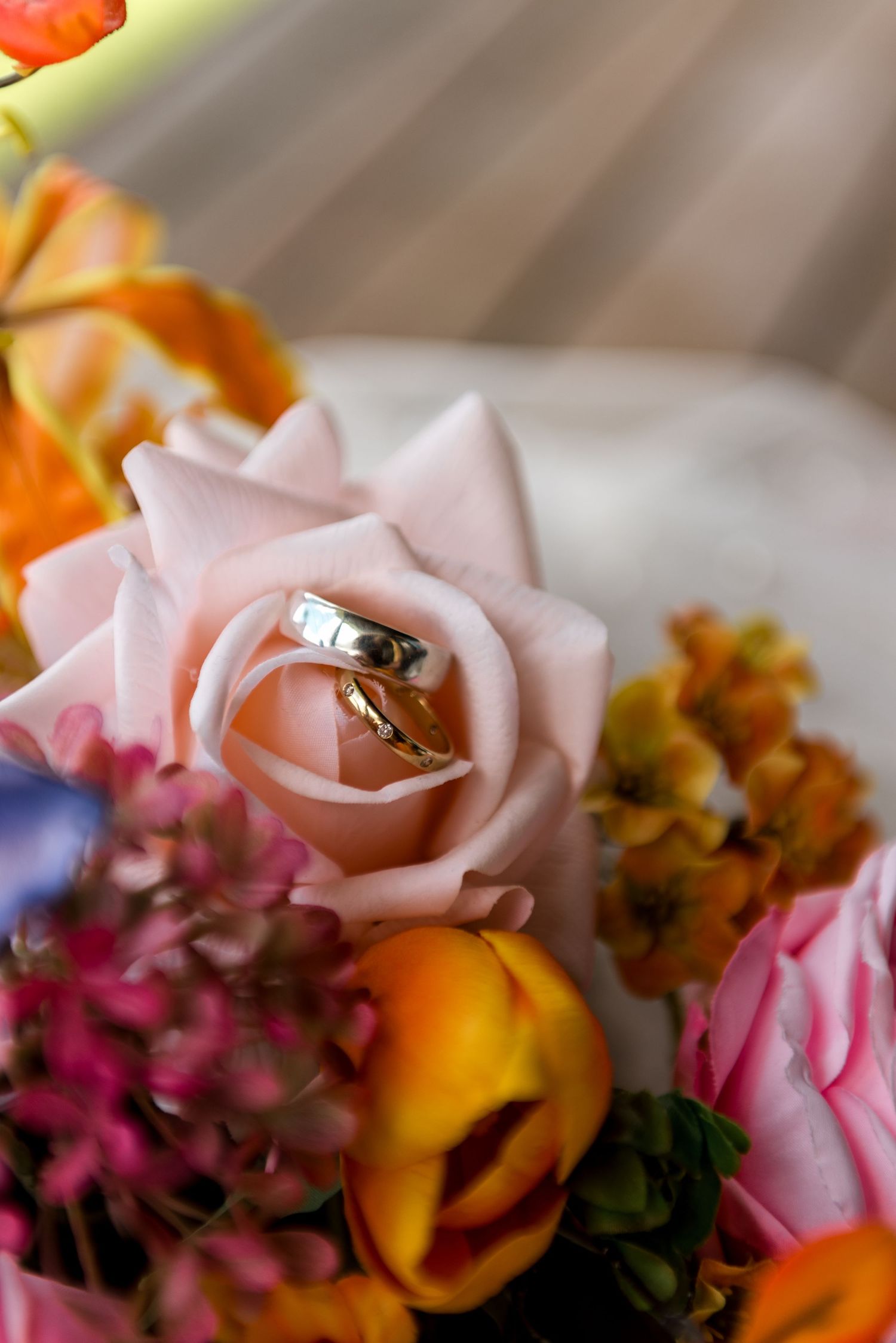 Two gold wedding bands nestled inside a pink rose surrounded by a colorful bridal bouquet.
