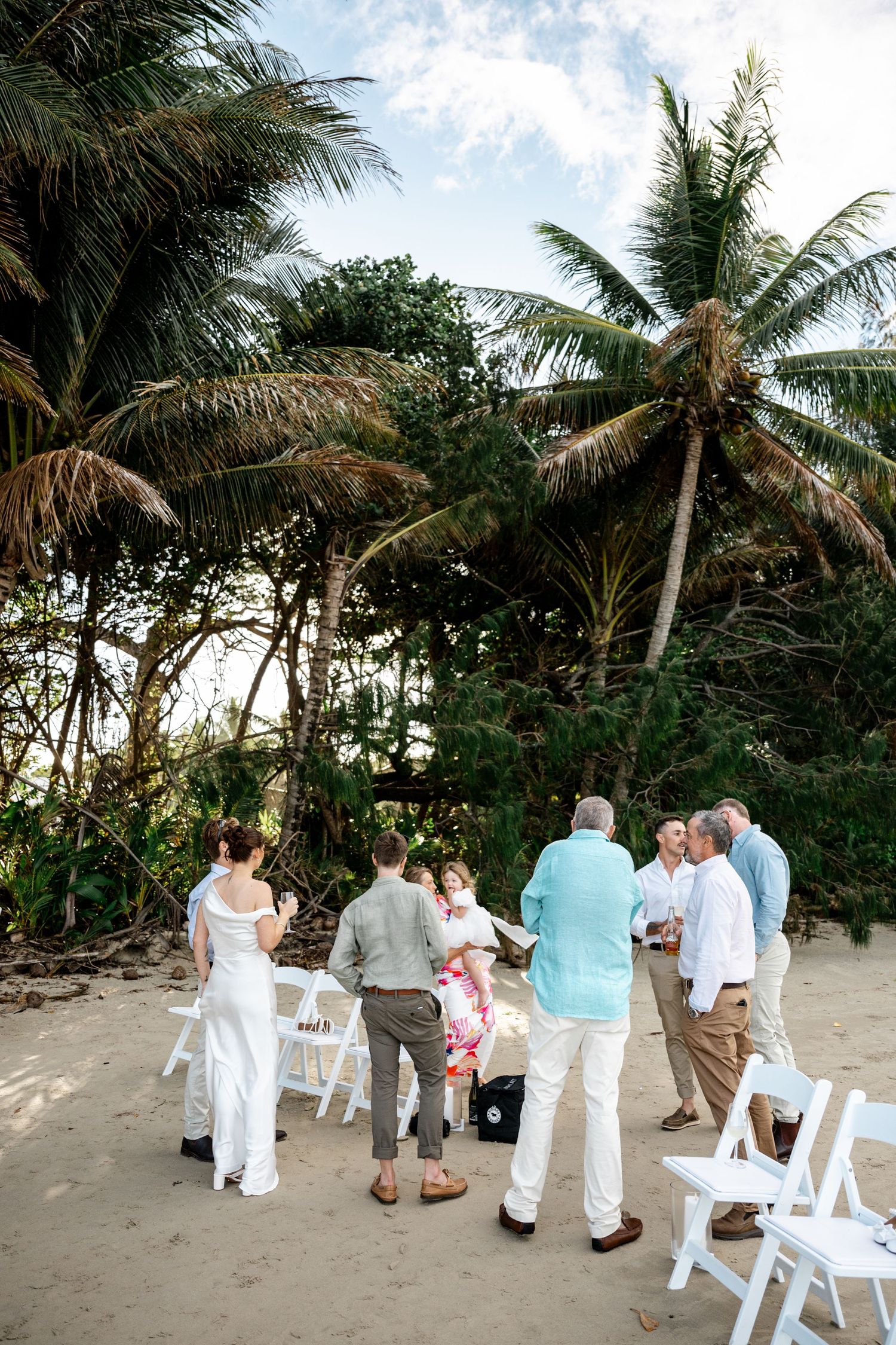 Small intimate beach wedding ceremony with guests gathered under tall palm trees on sandy shore at Four Mile Beach, Port Douglas.